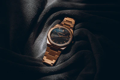 A gold watch rests on a dark gray fabric.
