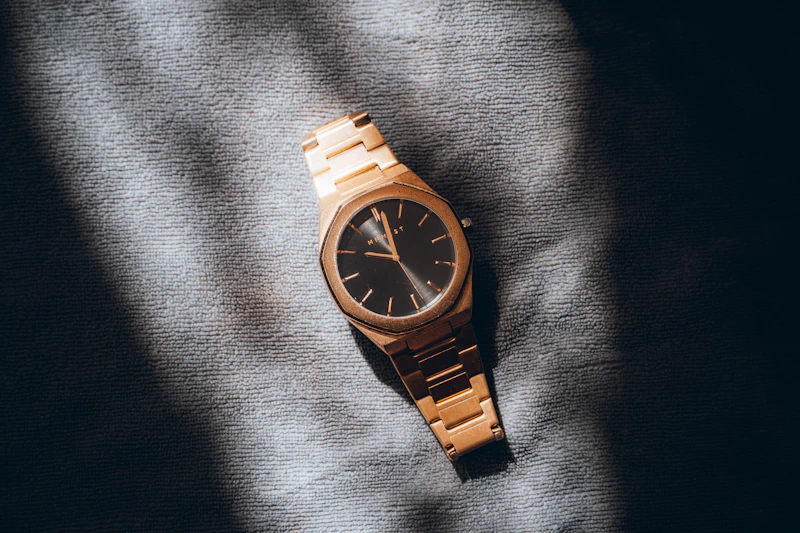 A gold watch with a black face rests on fabric.