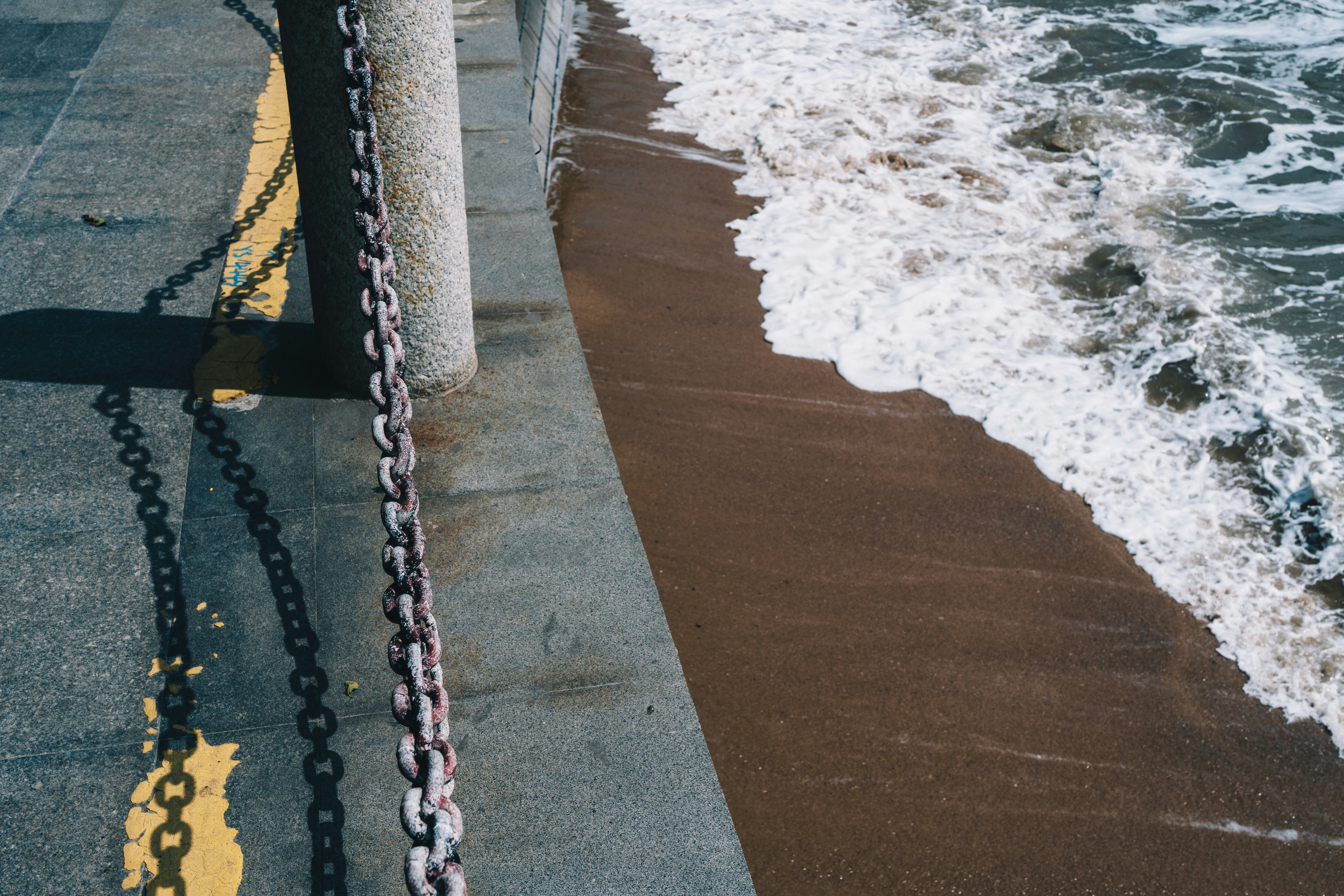 Waves crashing on a sandy beach next to a pier.