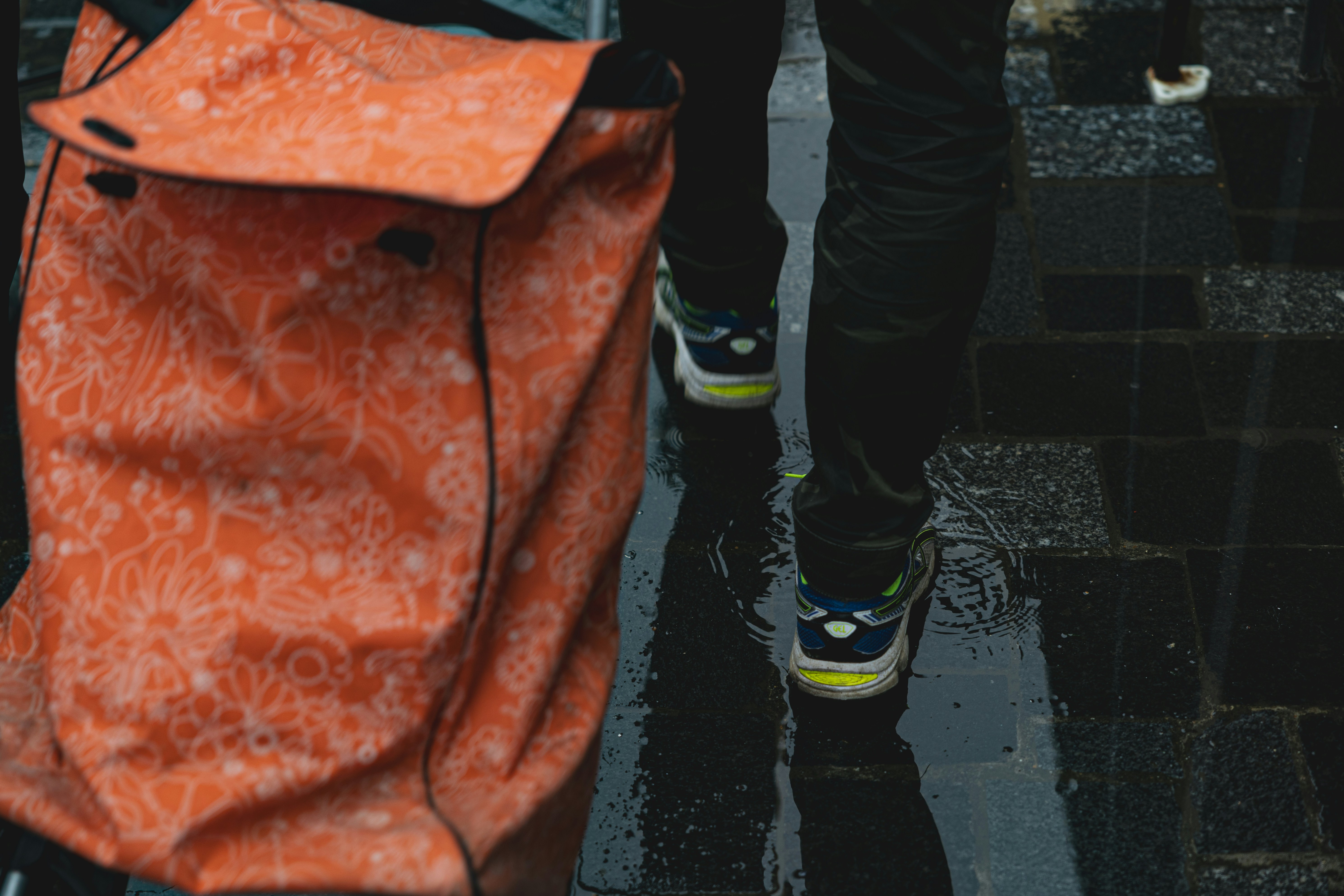 Person walking with an orange bag on wet pavement.