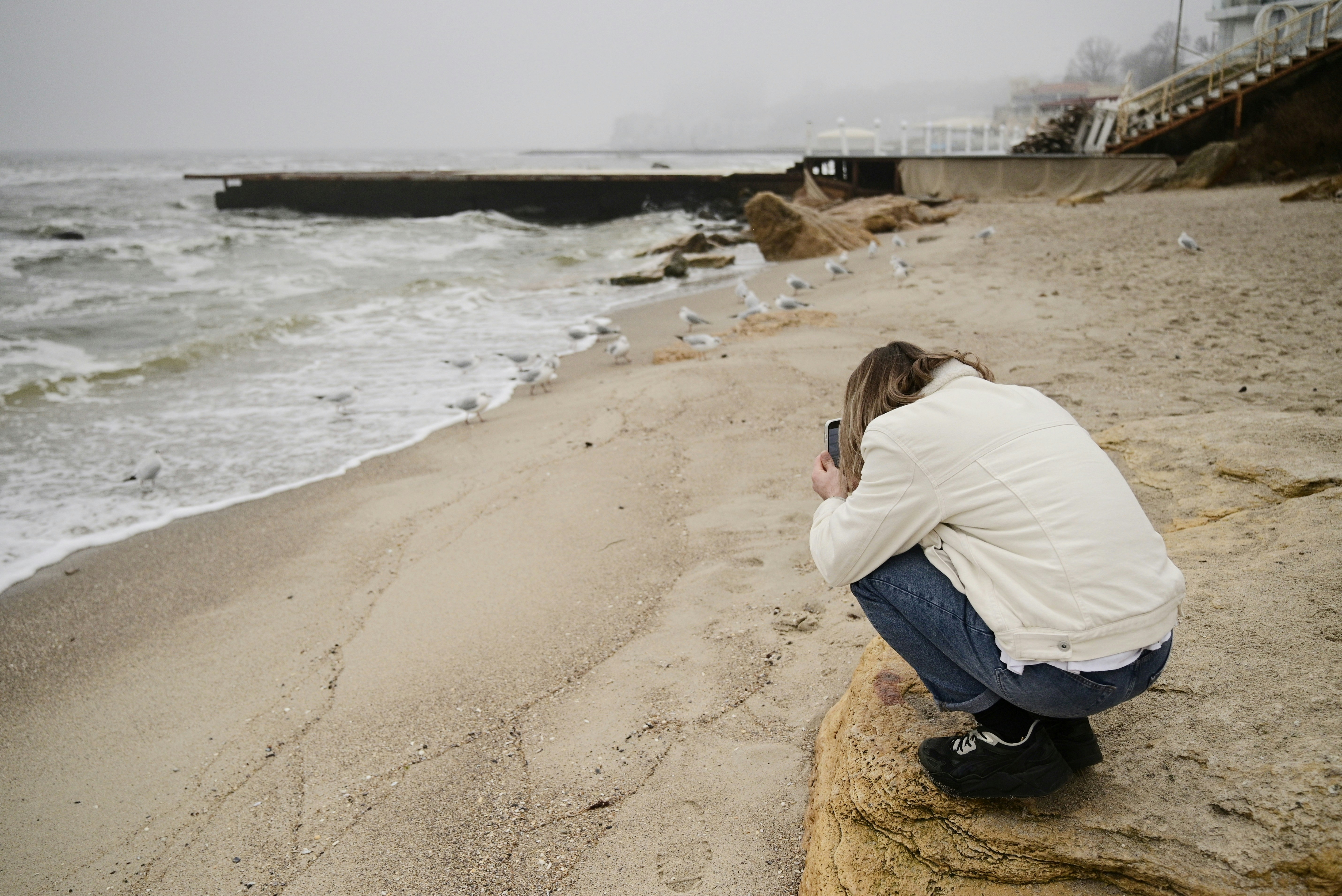 Femme photographiant une plage orageuse avec des vagues qui s’écrasent.