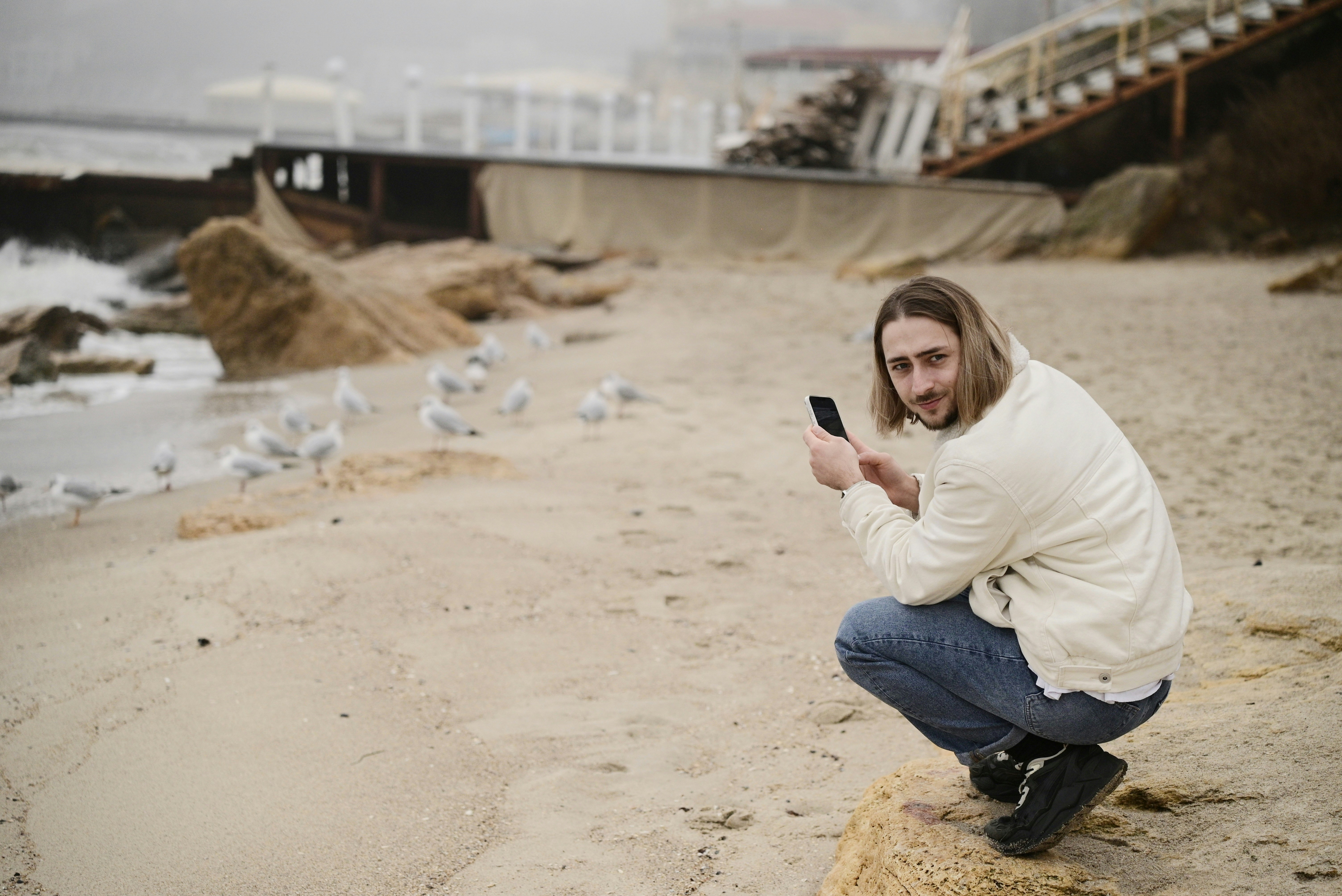 Un homme au téléphone photographie des mouettes sur une plage de sable.