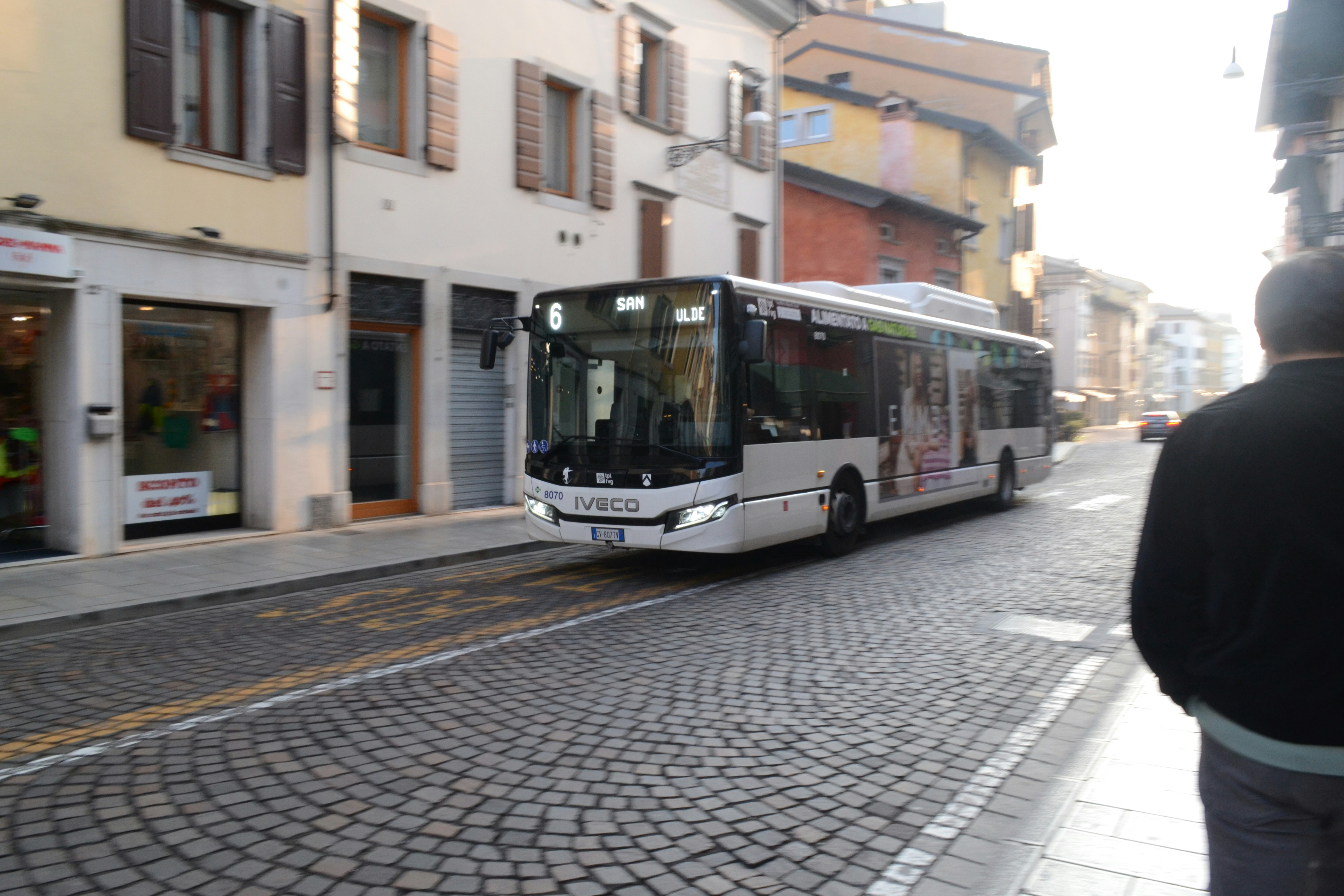 A modern white bus drives down a cobblestone street.
