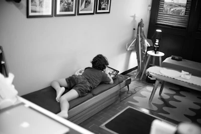 Child lying on a daybed looking at a tablet.