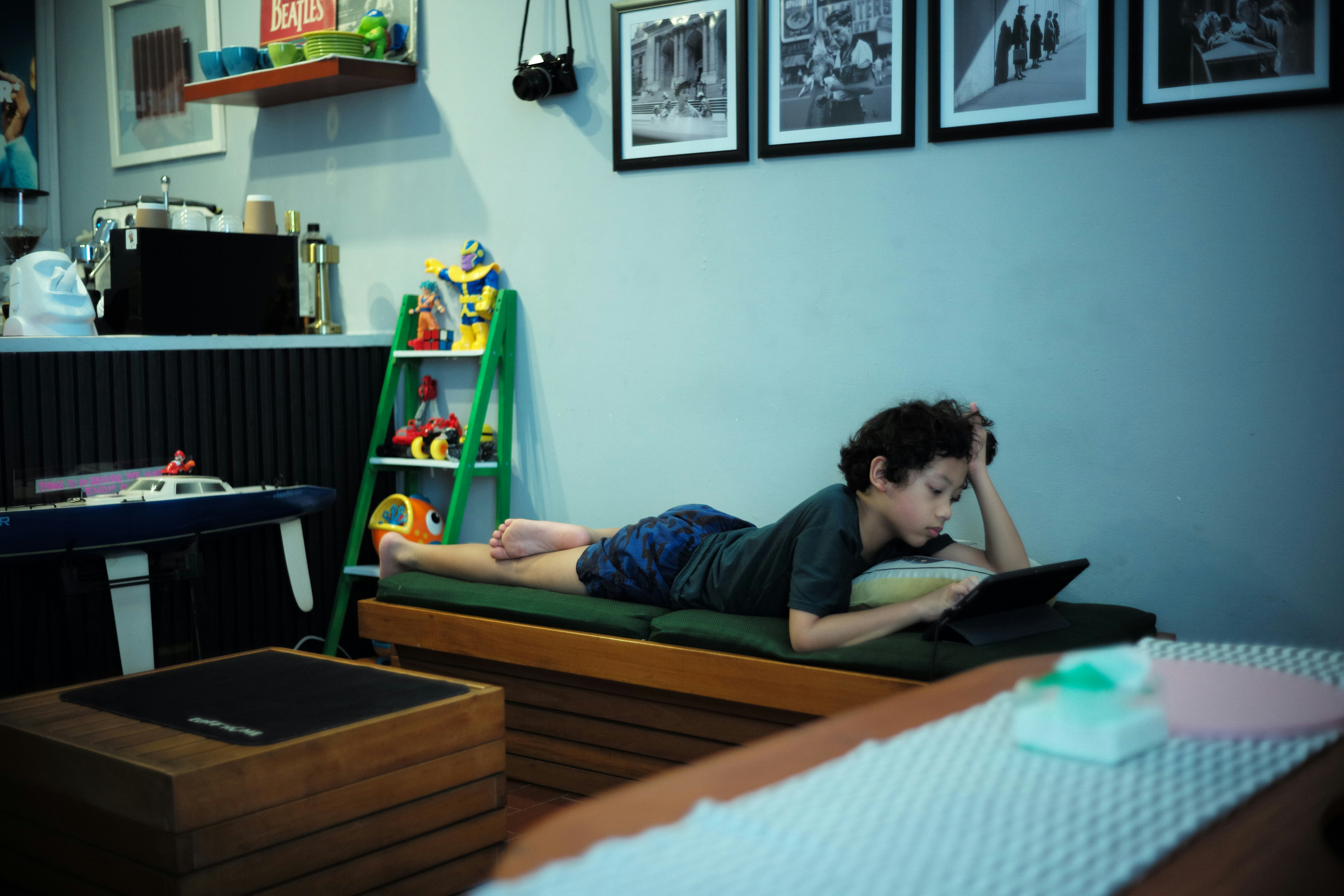 Garoto deitado no chão usando tablet em um quarto pouco iluminado.