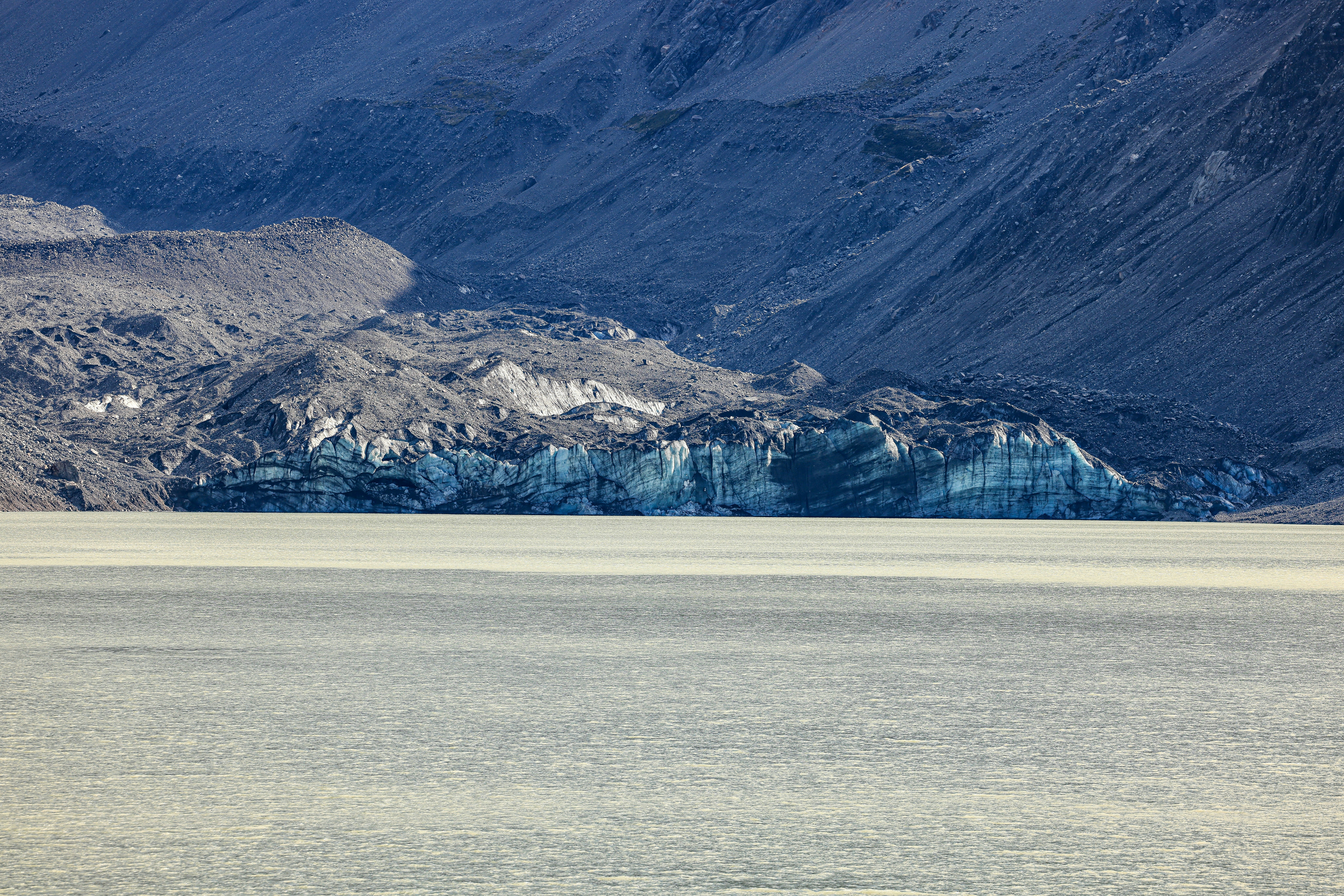 Glacier calving into a pale lake with mountains behind.