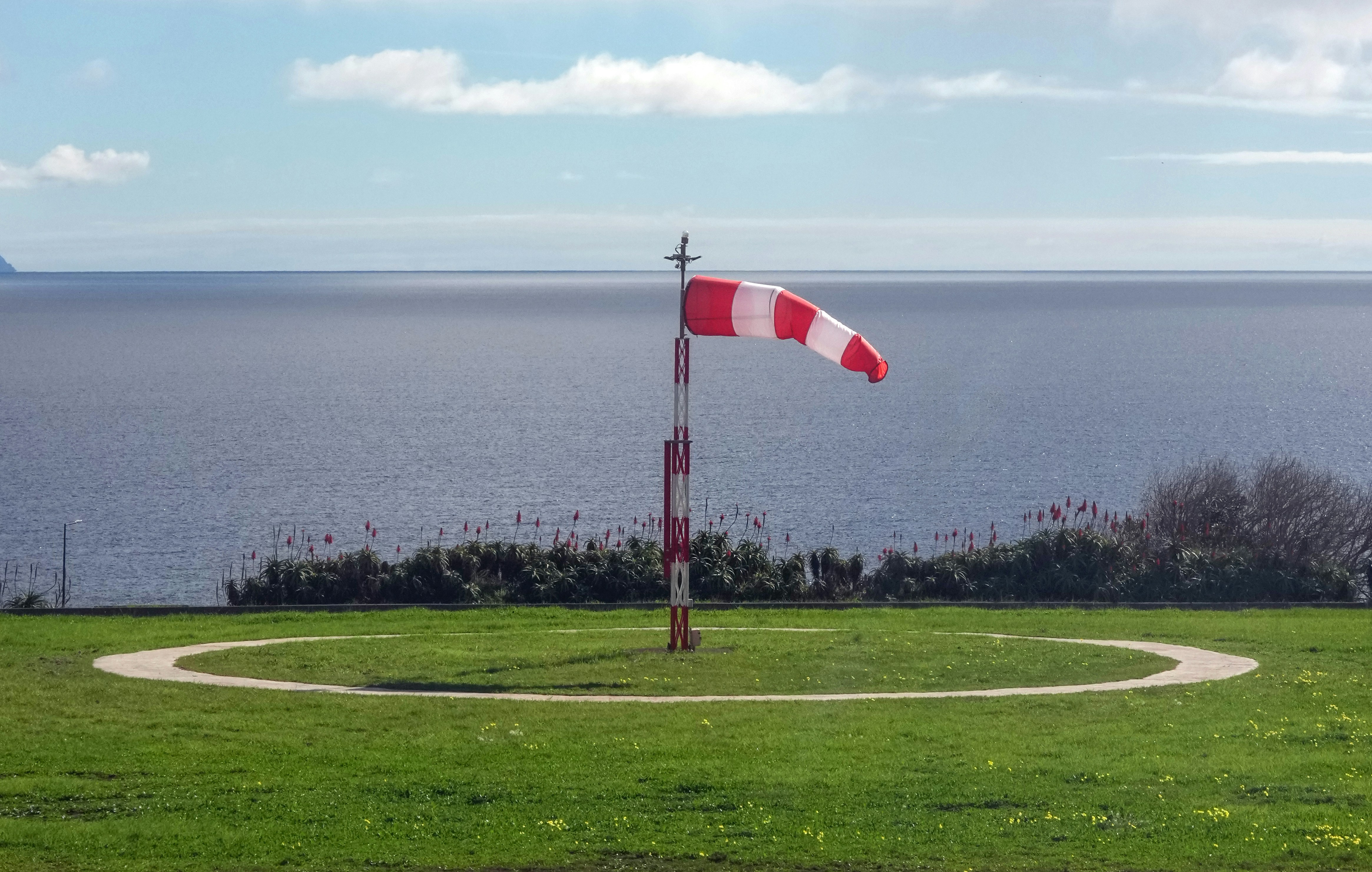 Red and white windsock on a pole by the sea