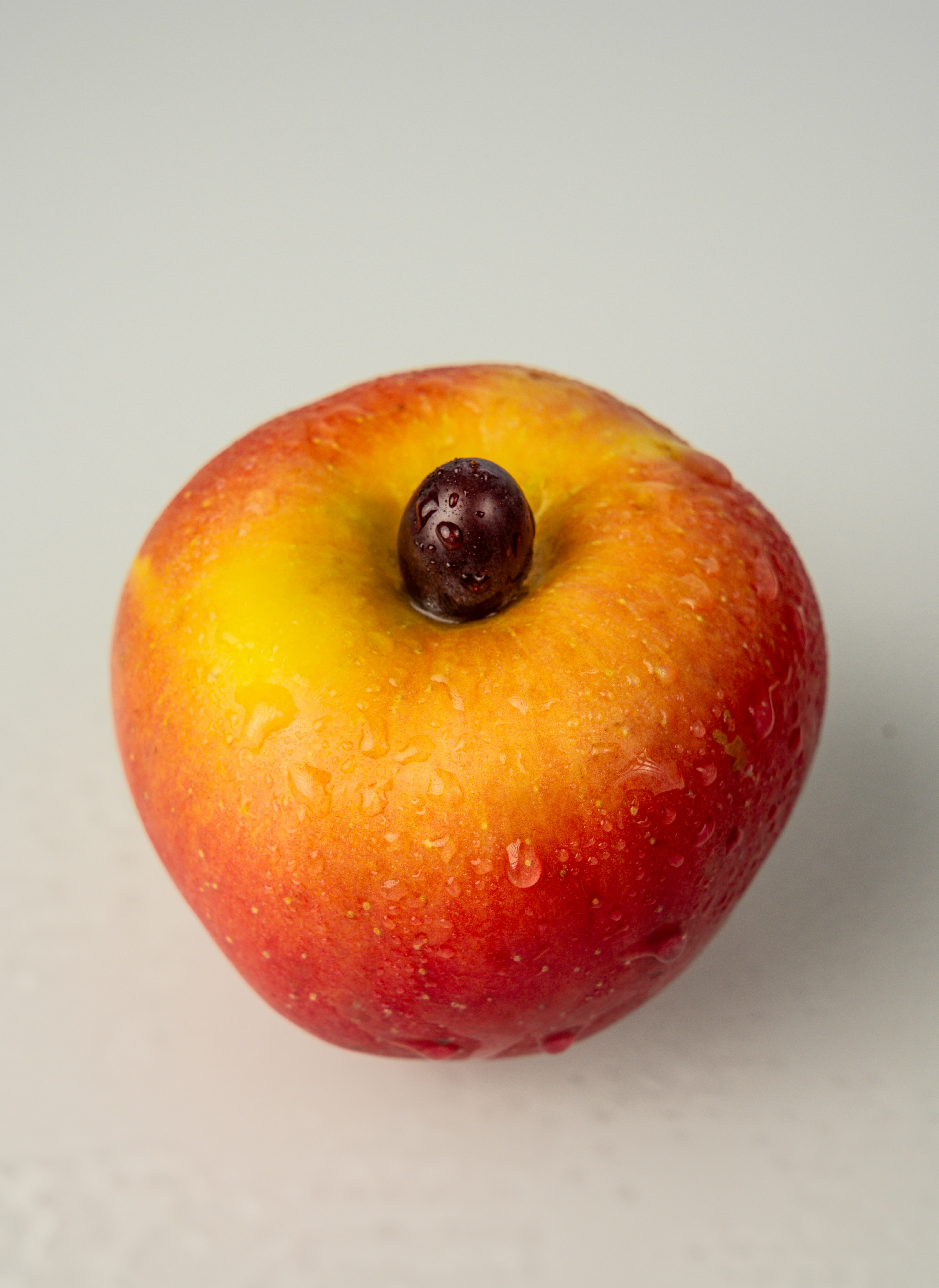 Uma maçã vermelha e amarela com uma uva no topo.