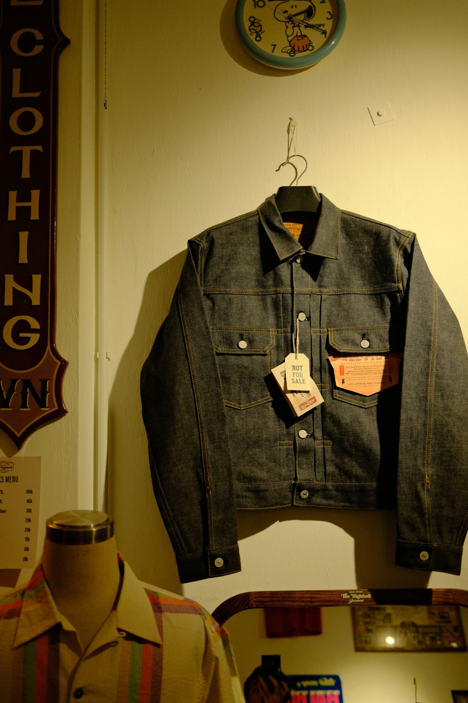 Dark denim jacket hanging on a wall with tags