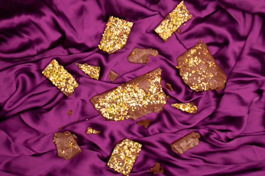 Broken chocolate pieces with nuts on purple satin fabric