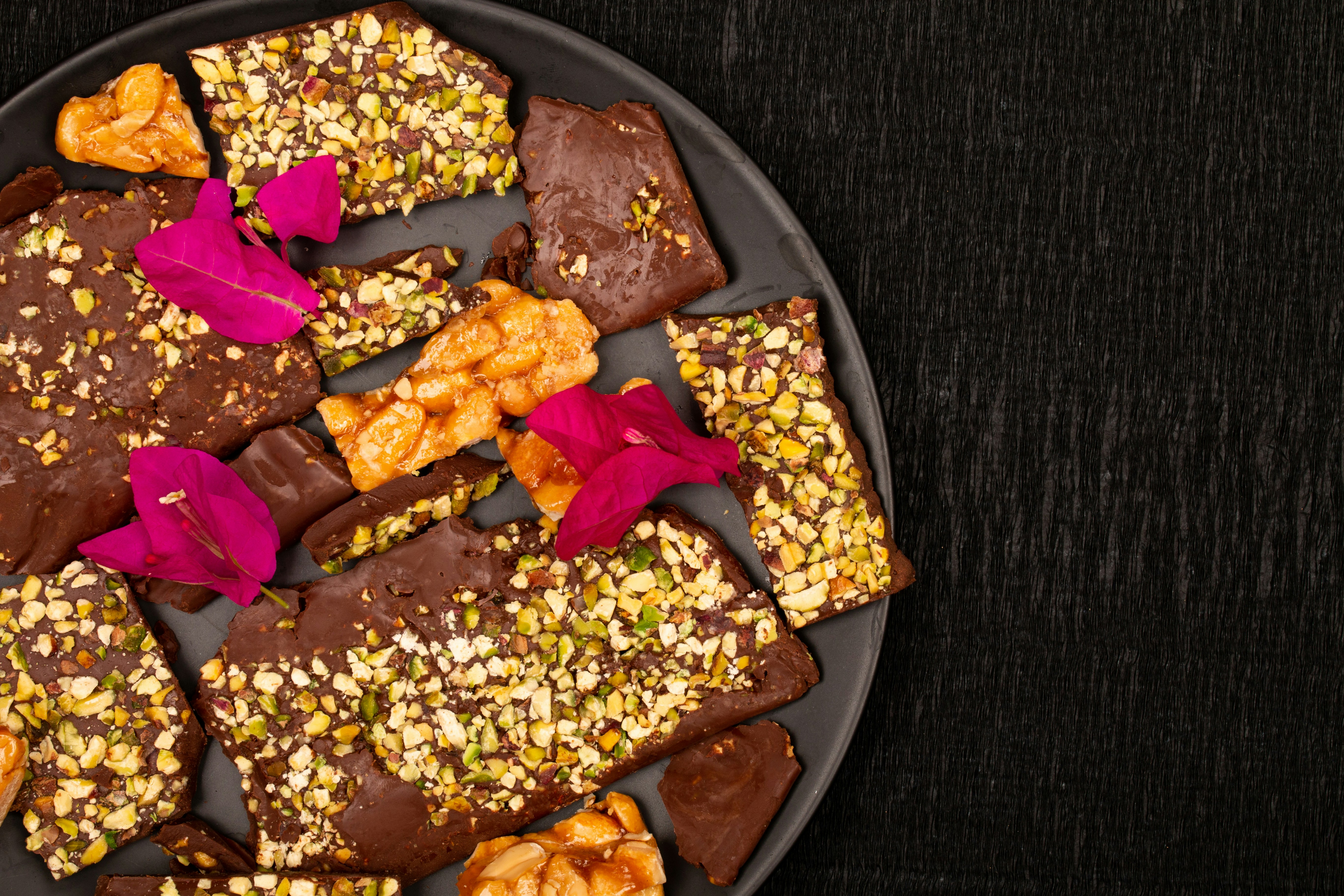 Corteza de chocolate con frutos secos y flores rosas en un plato