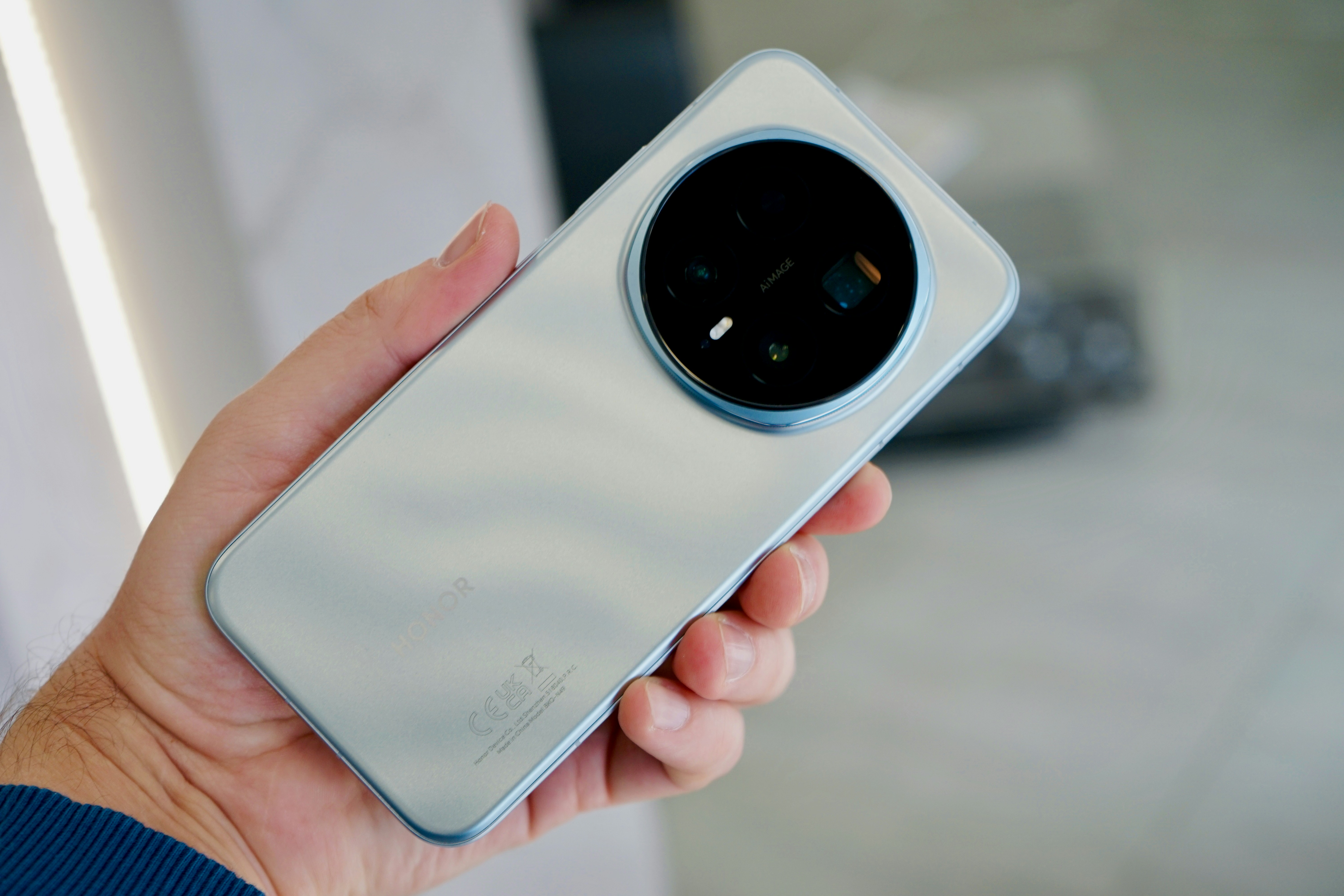 Mão segurando um smartphone prateado com uma grande lente de câmera.