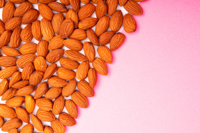 A pile of almonds scattered on a pink background.