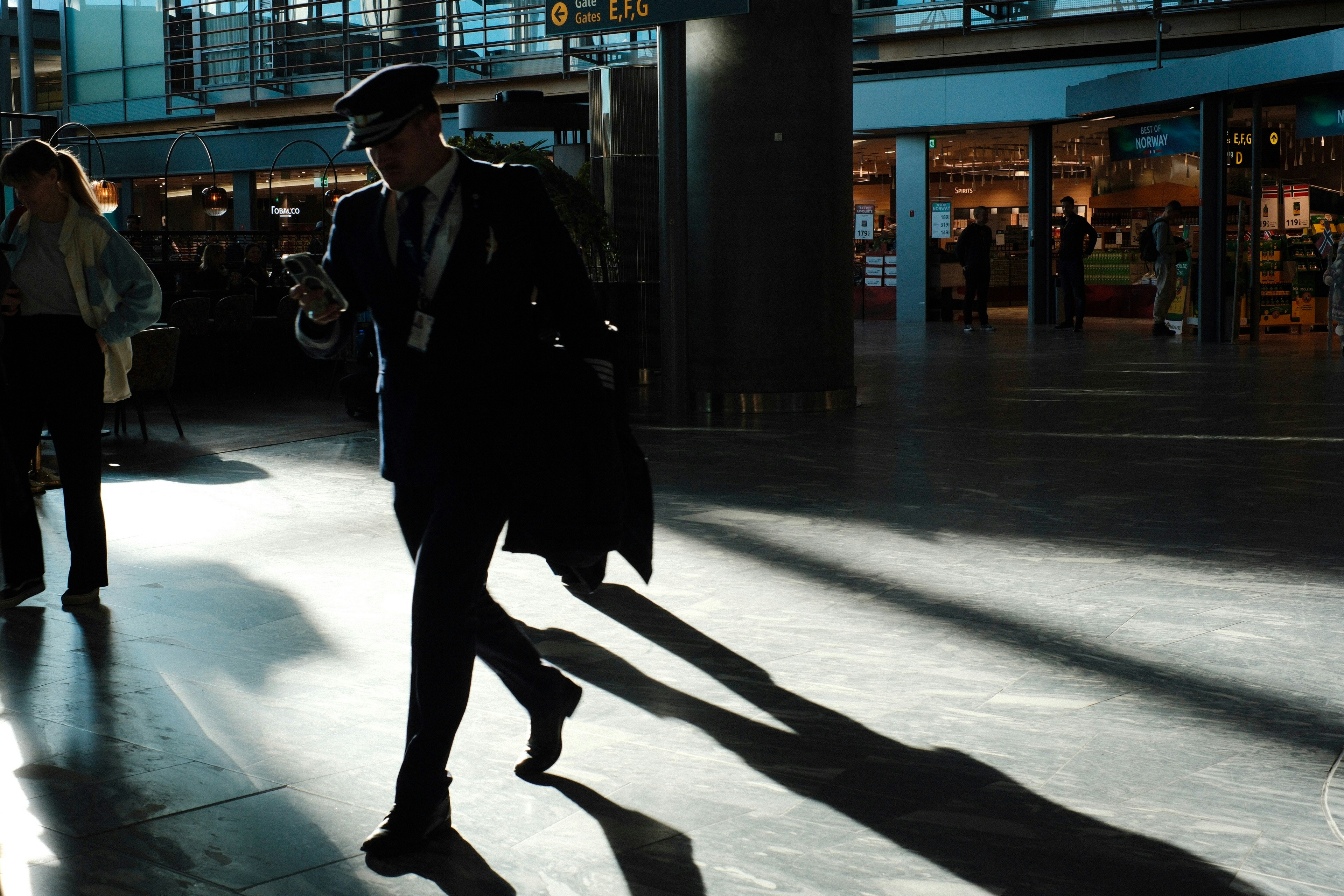 햇살이 가득한 현대식 공항 터미널을 걷는 남자.