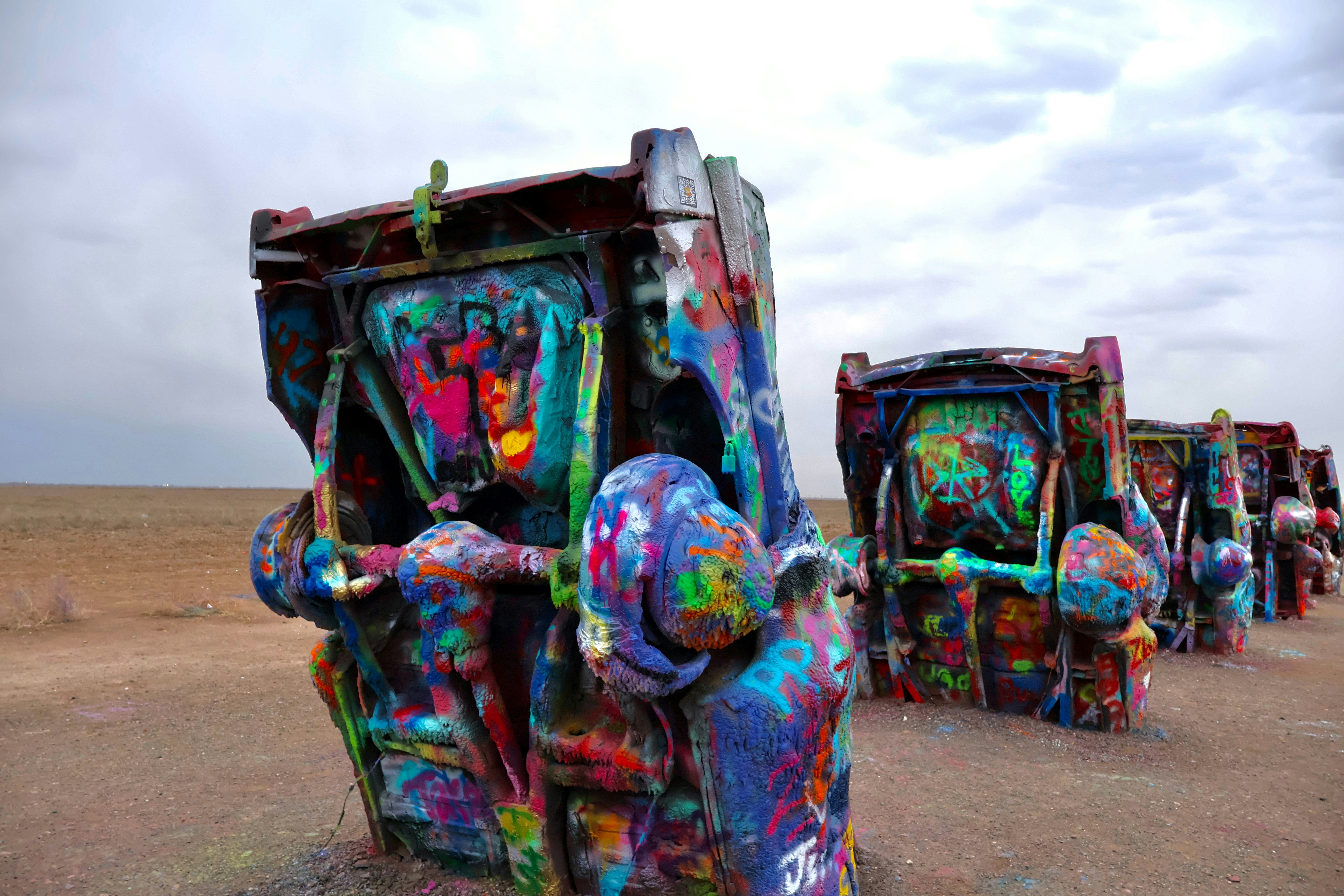 Graffiti-covered cars buried nose-down in desert landscape.