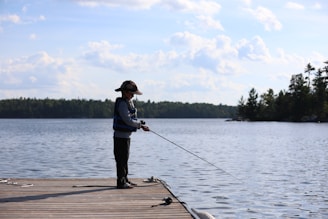 A person fishing from a wooden dock on a lake.