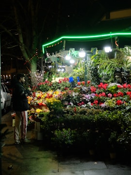 Person browsing a vibrant flower stand at night.