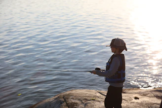 A young boy fishes by a calm lake