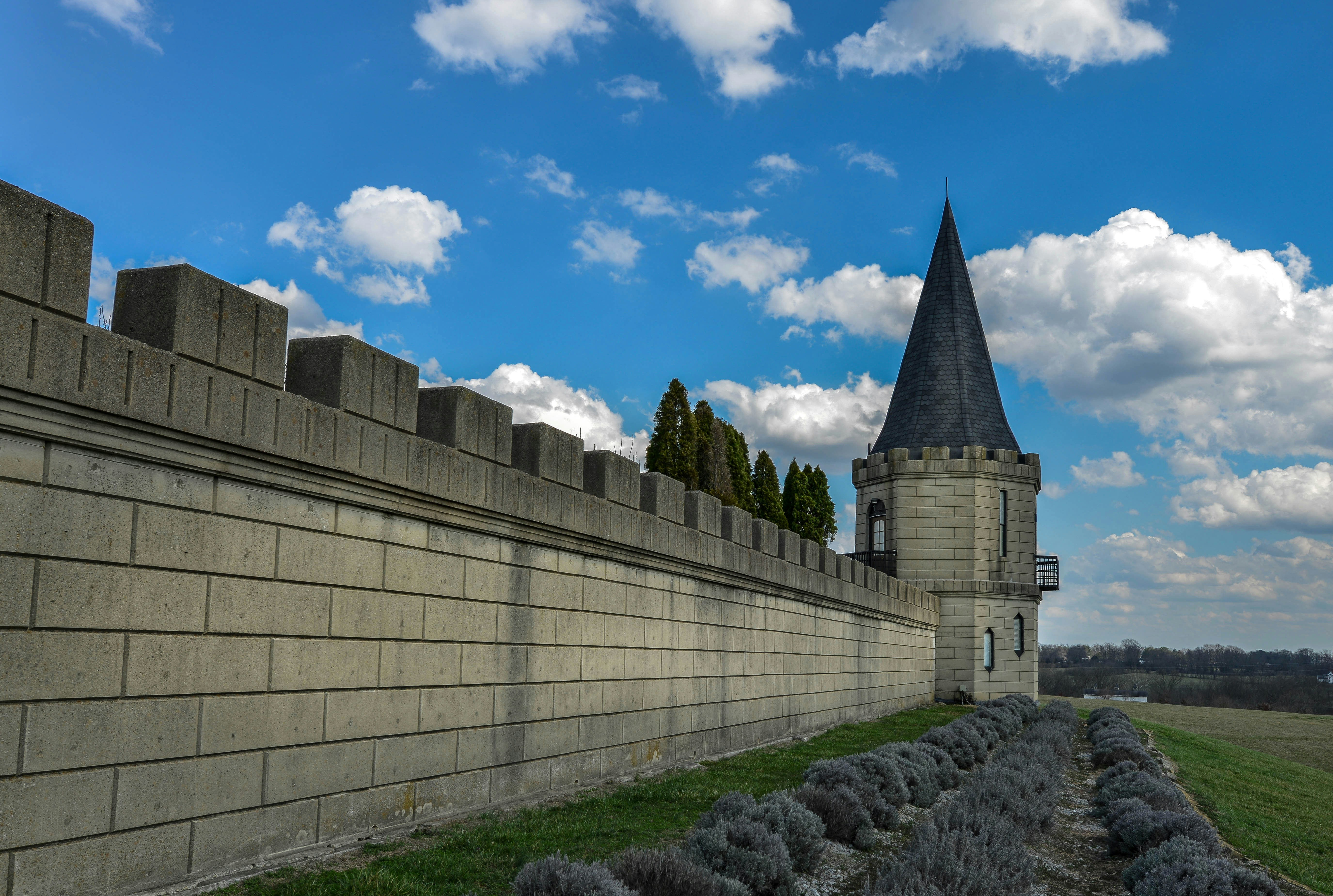 Stone castle wall with a pointed tower under blue sky.