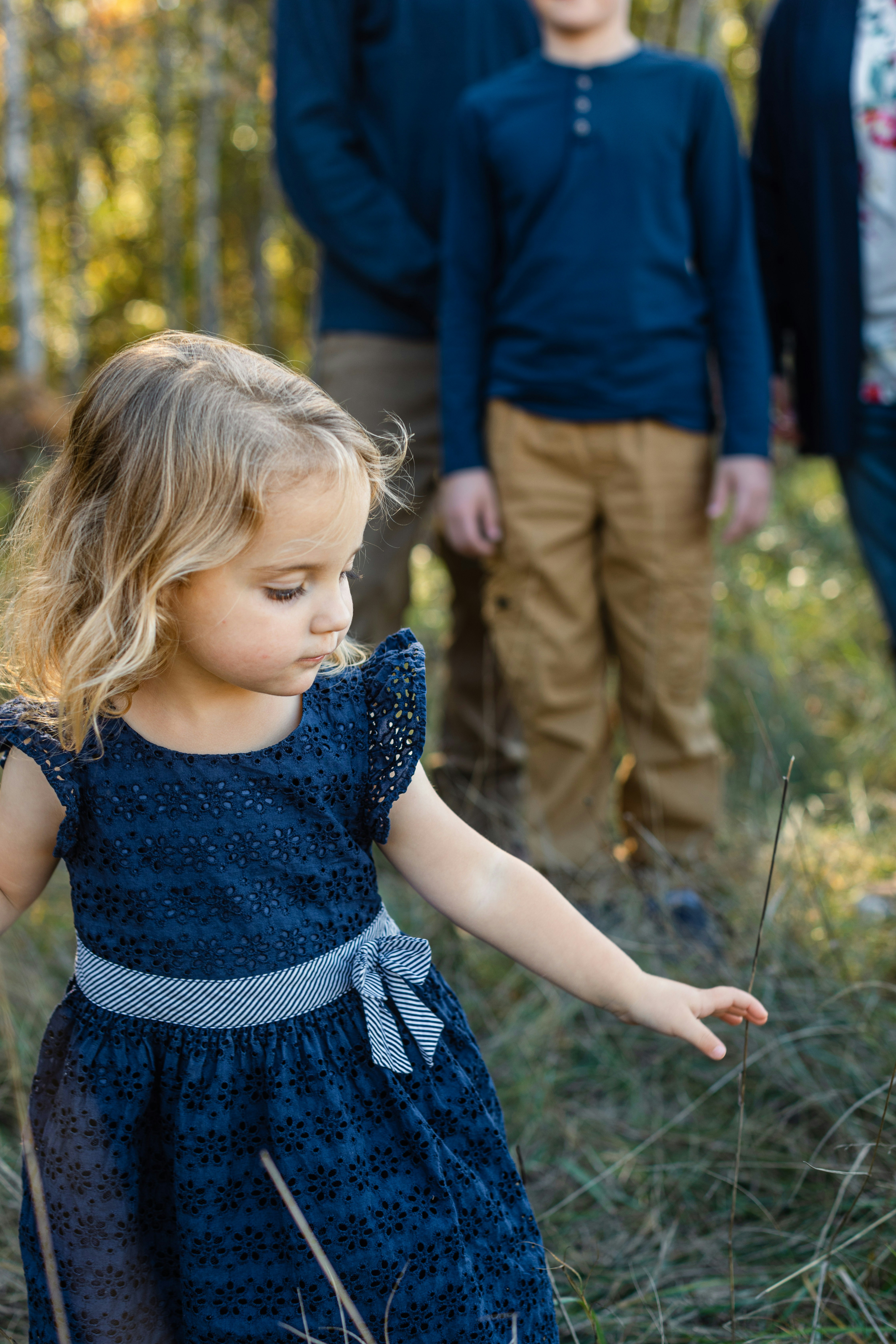 Une jeune fille en robe bleue tend la main vers l’herbe.