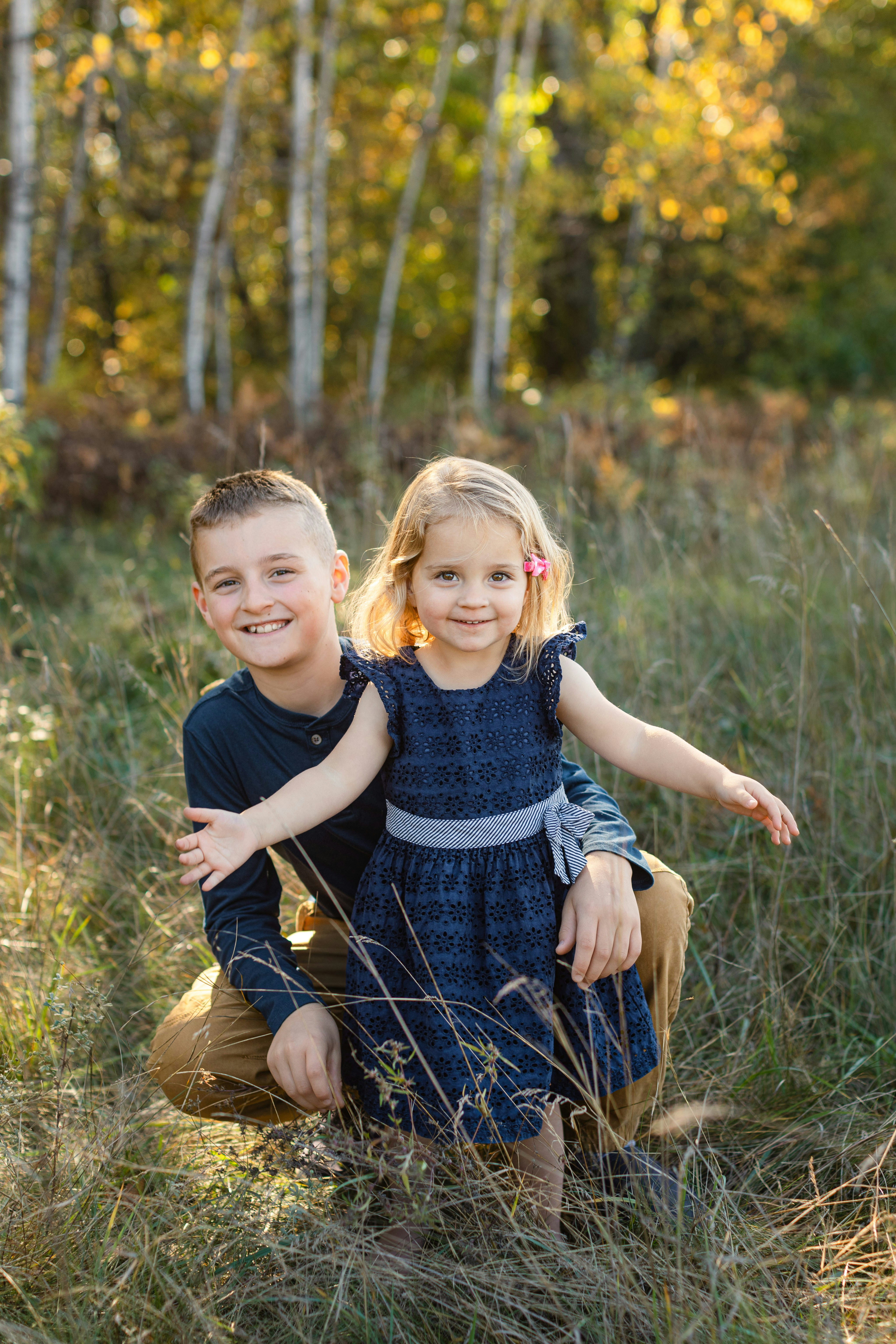 Frère et sœur souriant dans un champ d’herbe.