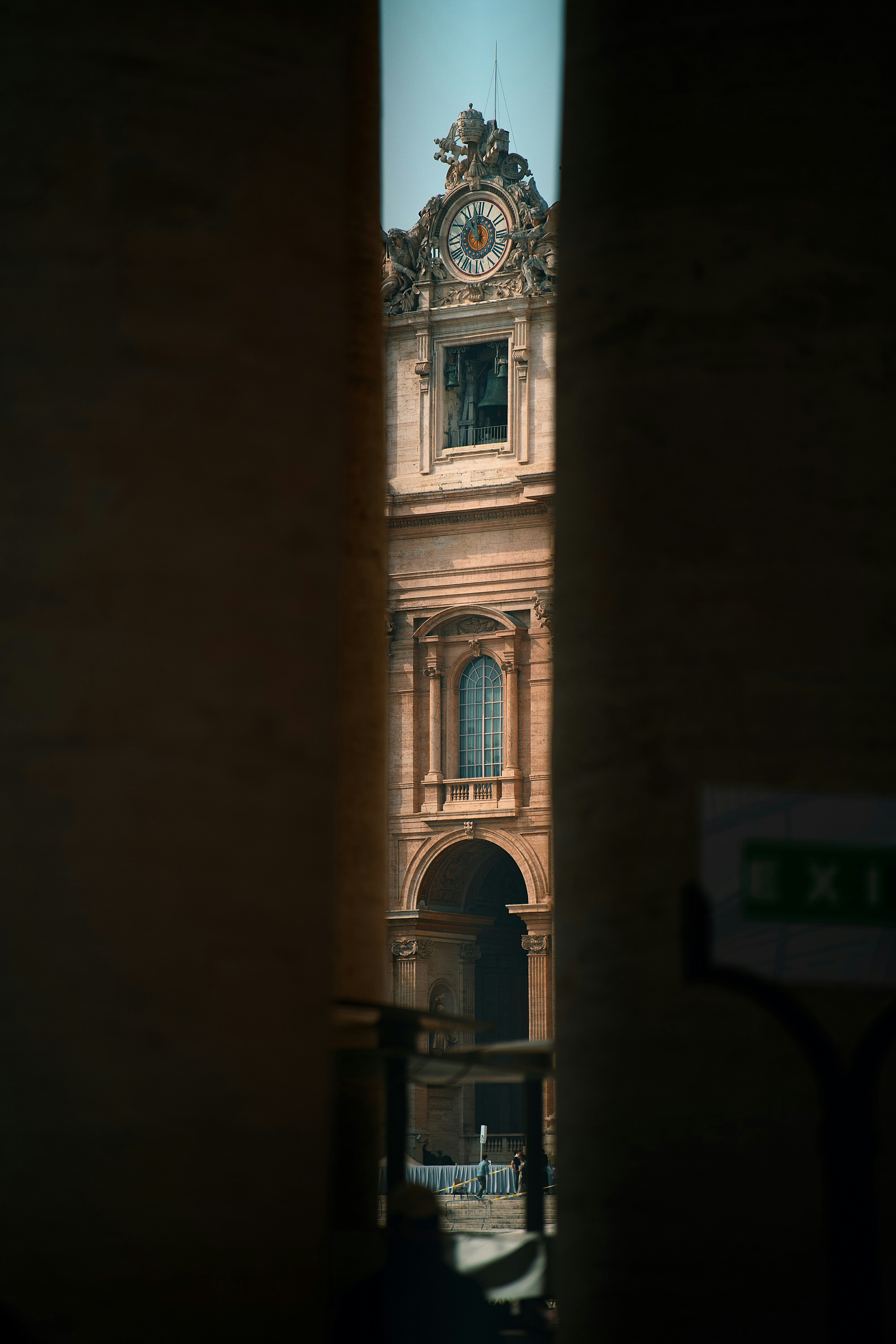 Ornate building facade with clock tower viewed through columns.