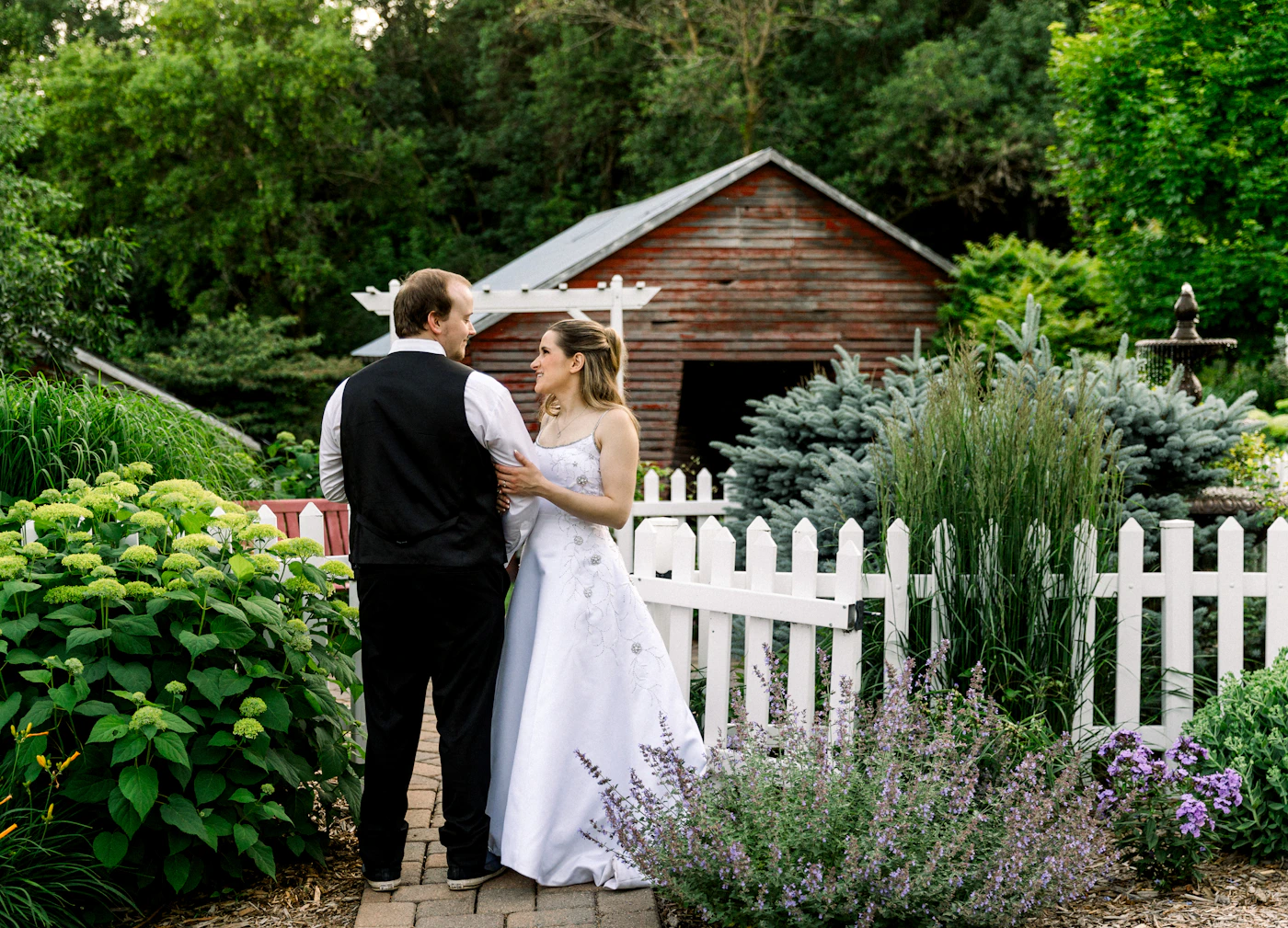 Couple in elopement attire at a Prince Edward County vineyard with the grapevines on either side of them and the pastoral Ontario countryside visible behind