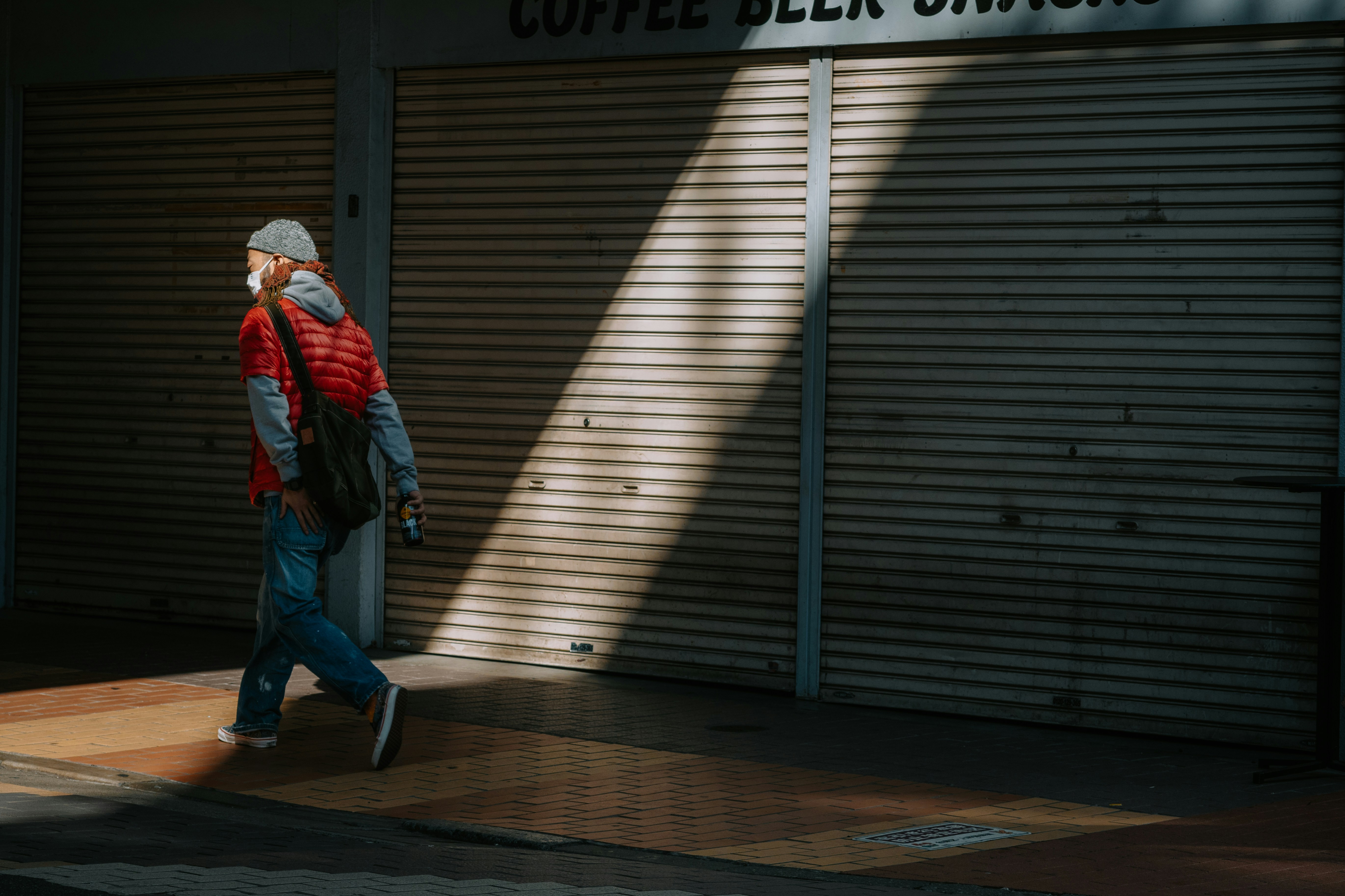 Man walks past closed storefront with striped shadows.