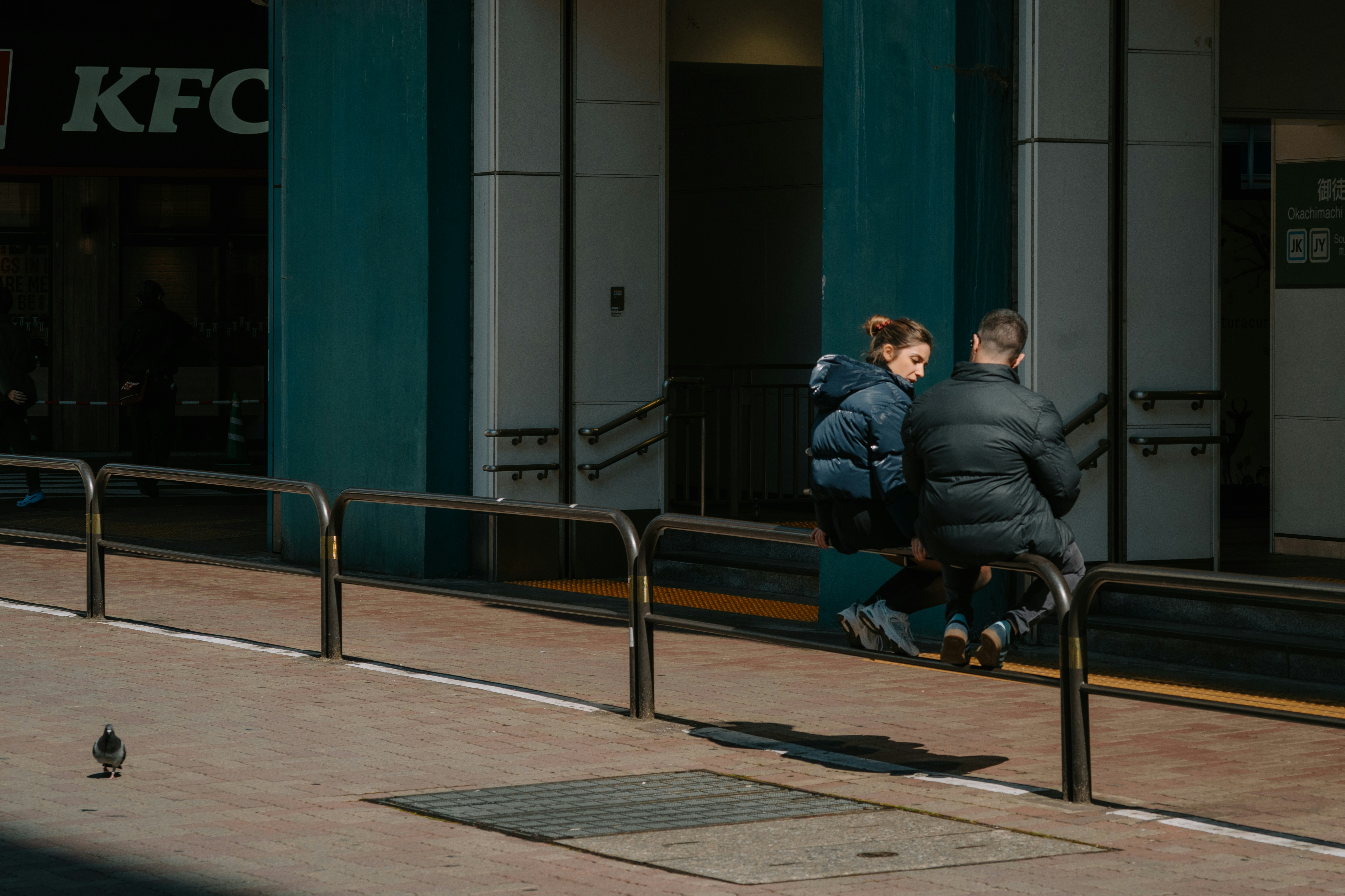 Two people sit on a ledge outside kfc.