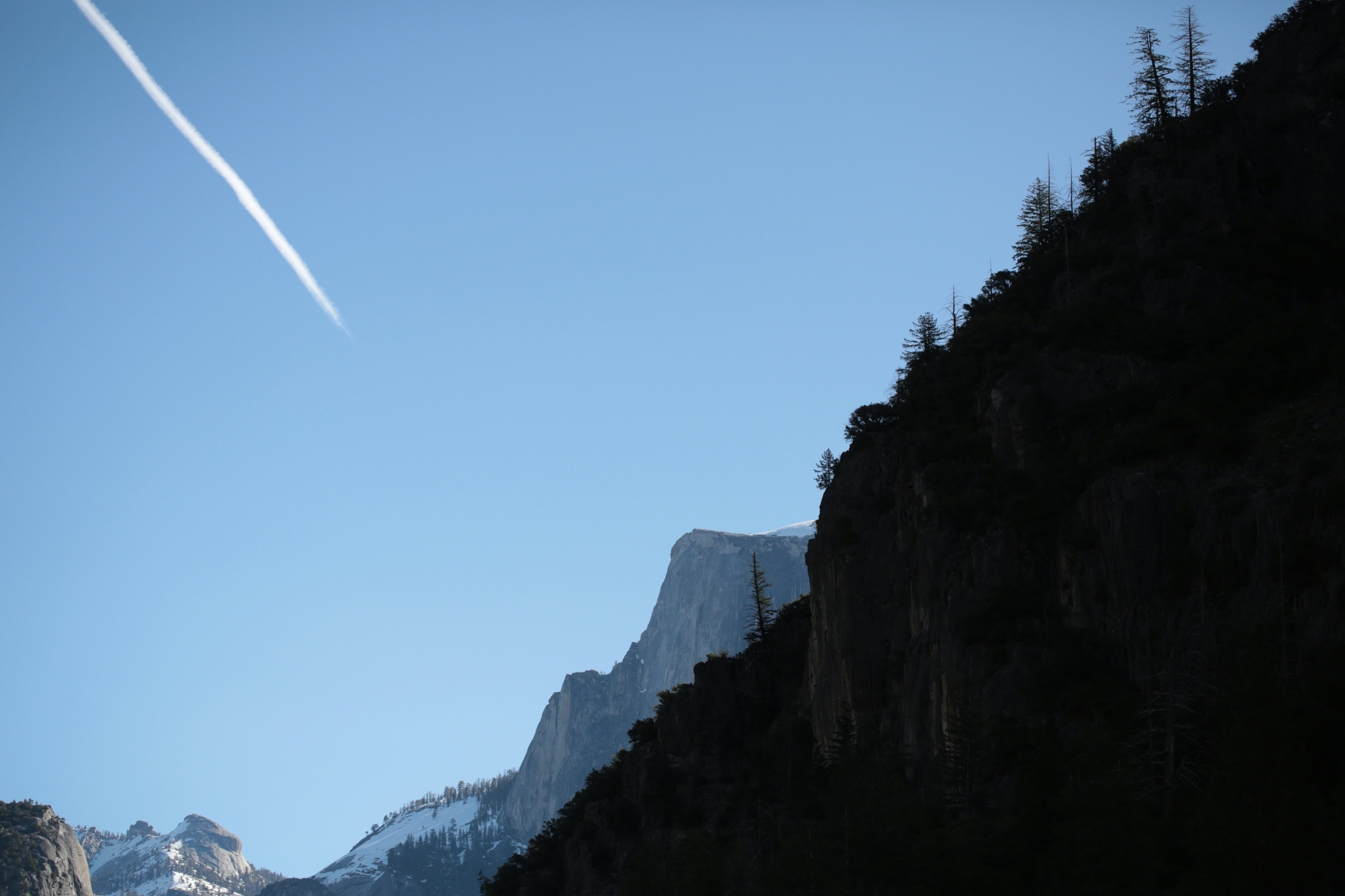 Jet trail crosses a clear blue sky over mountains.