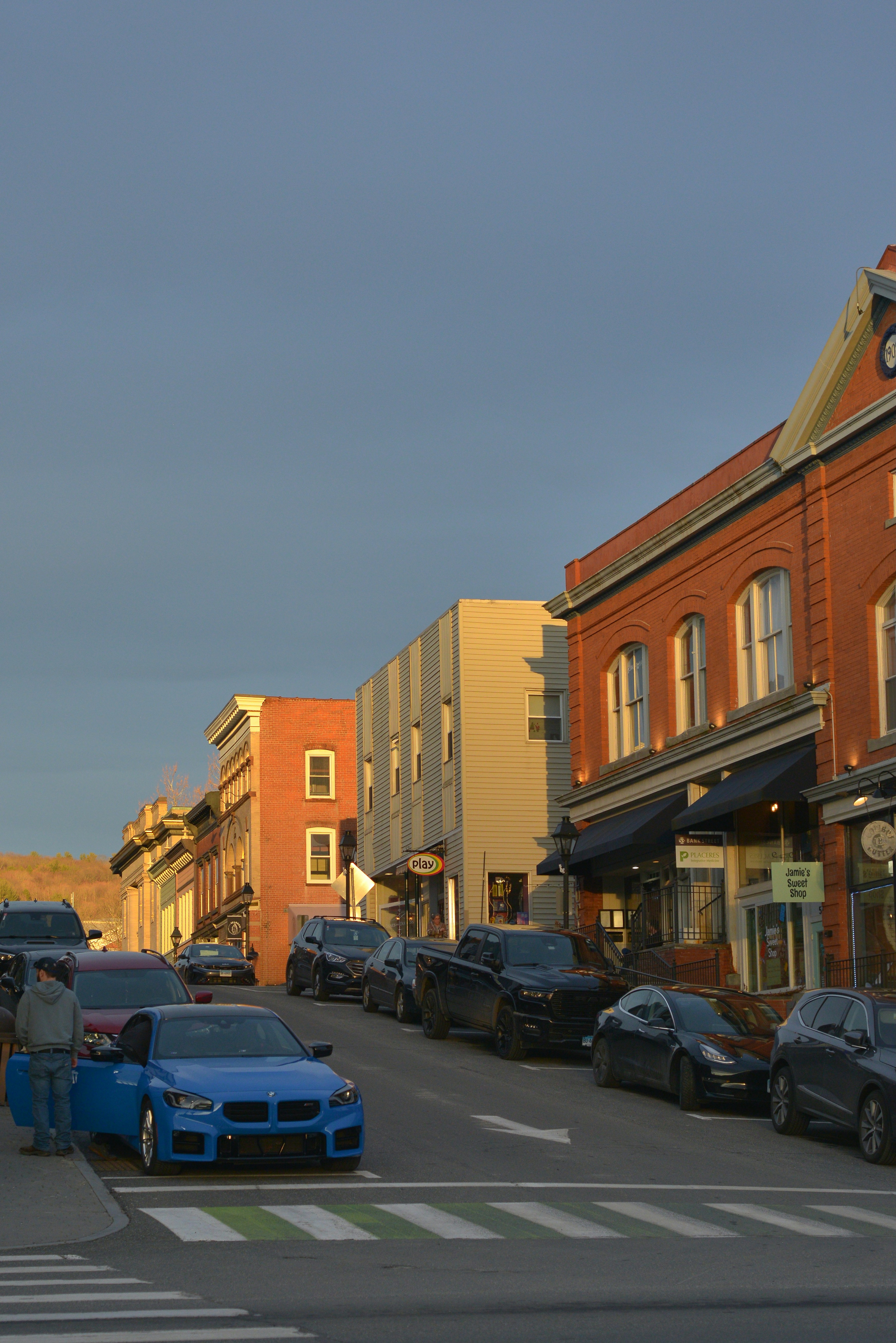 Straße mit geparkten Autos und Backsteingebäuden bei Sonnenuntergang.