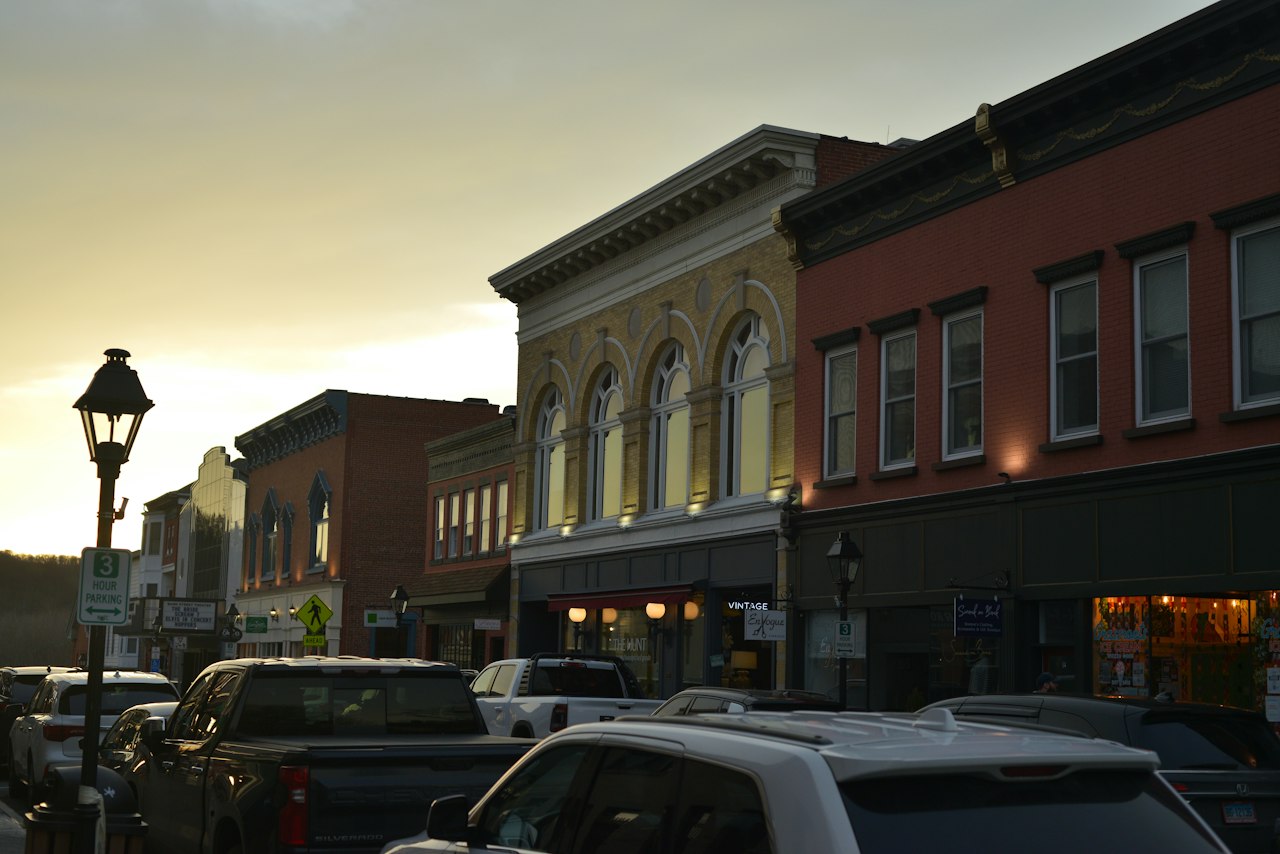 Downtown street at dusk with historic brick storefronts and parked cars.