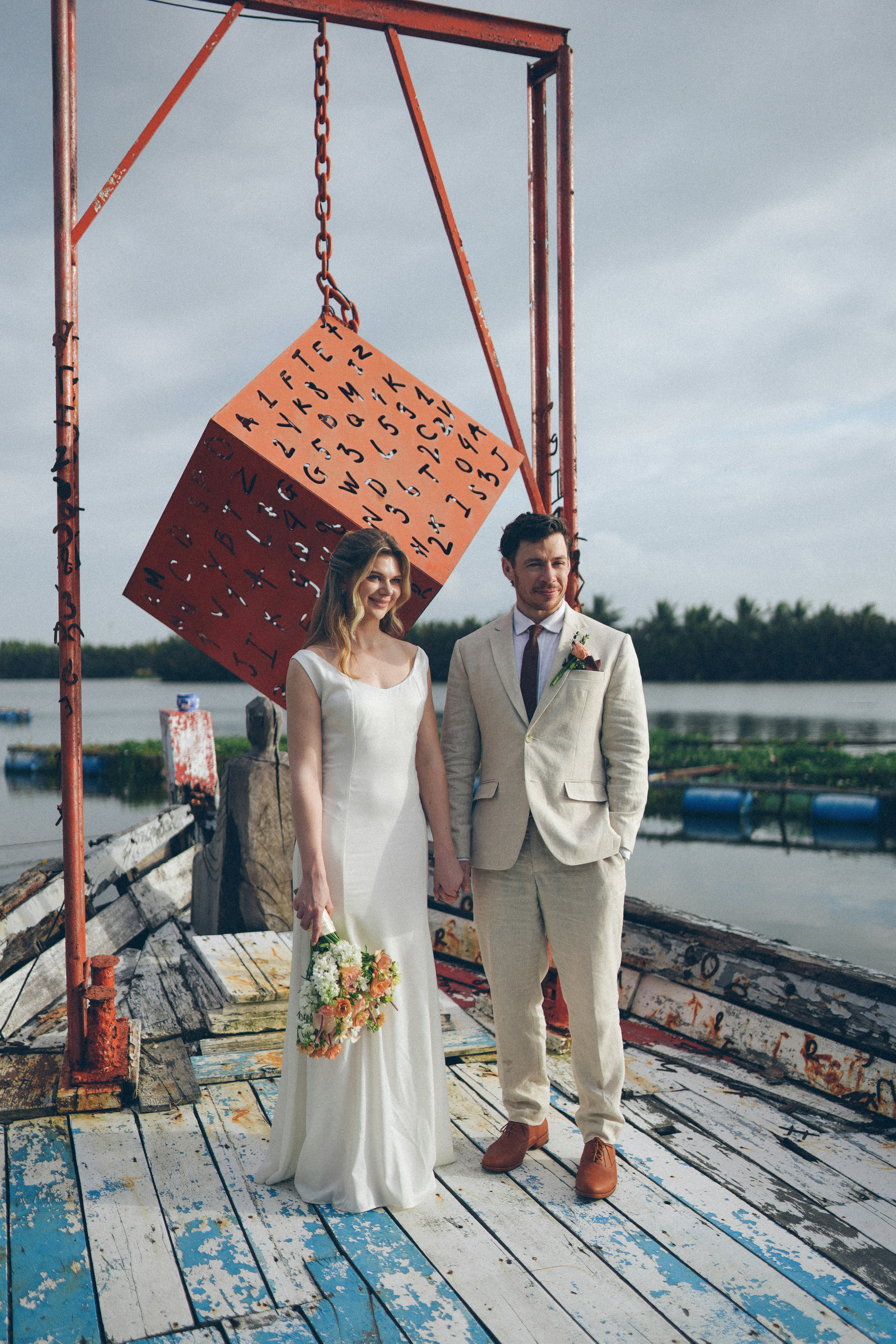 A bride and groom stand on a wooden dock.