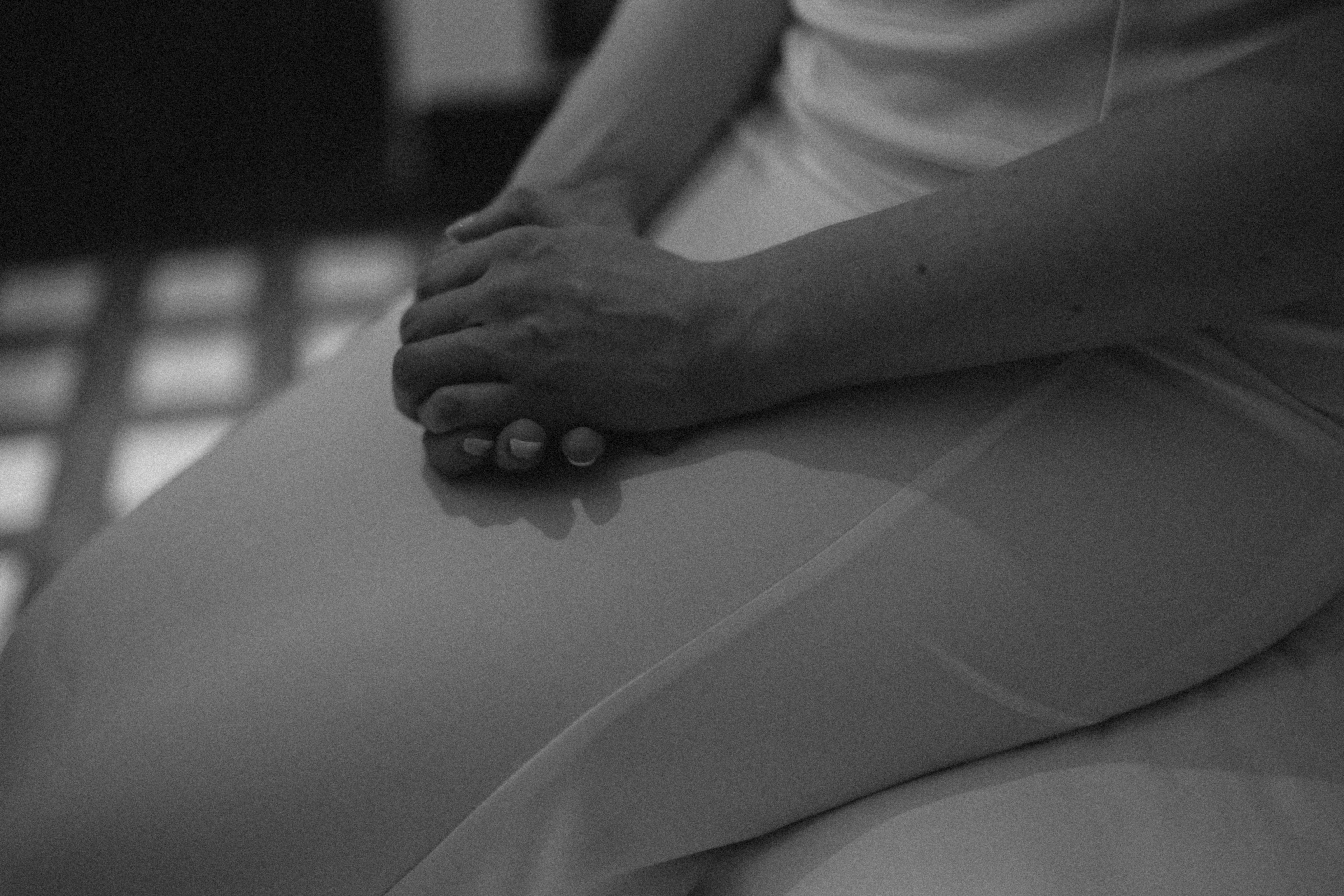 A person's hands clasped together resting on lap.