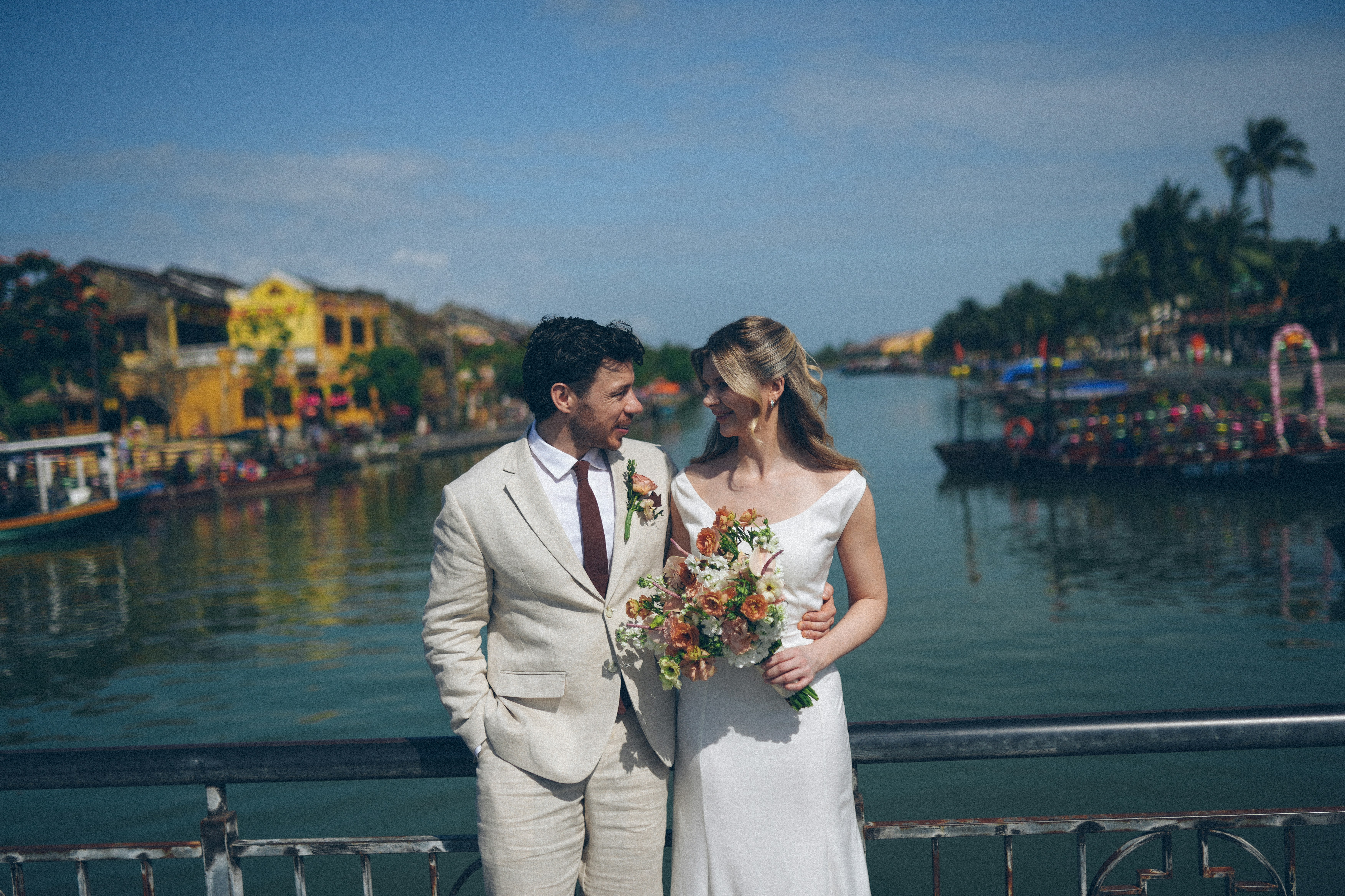 Newlyweds pose on a bridge overlooking a canal.