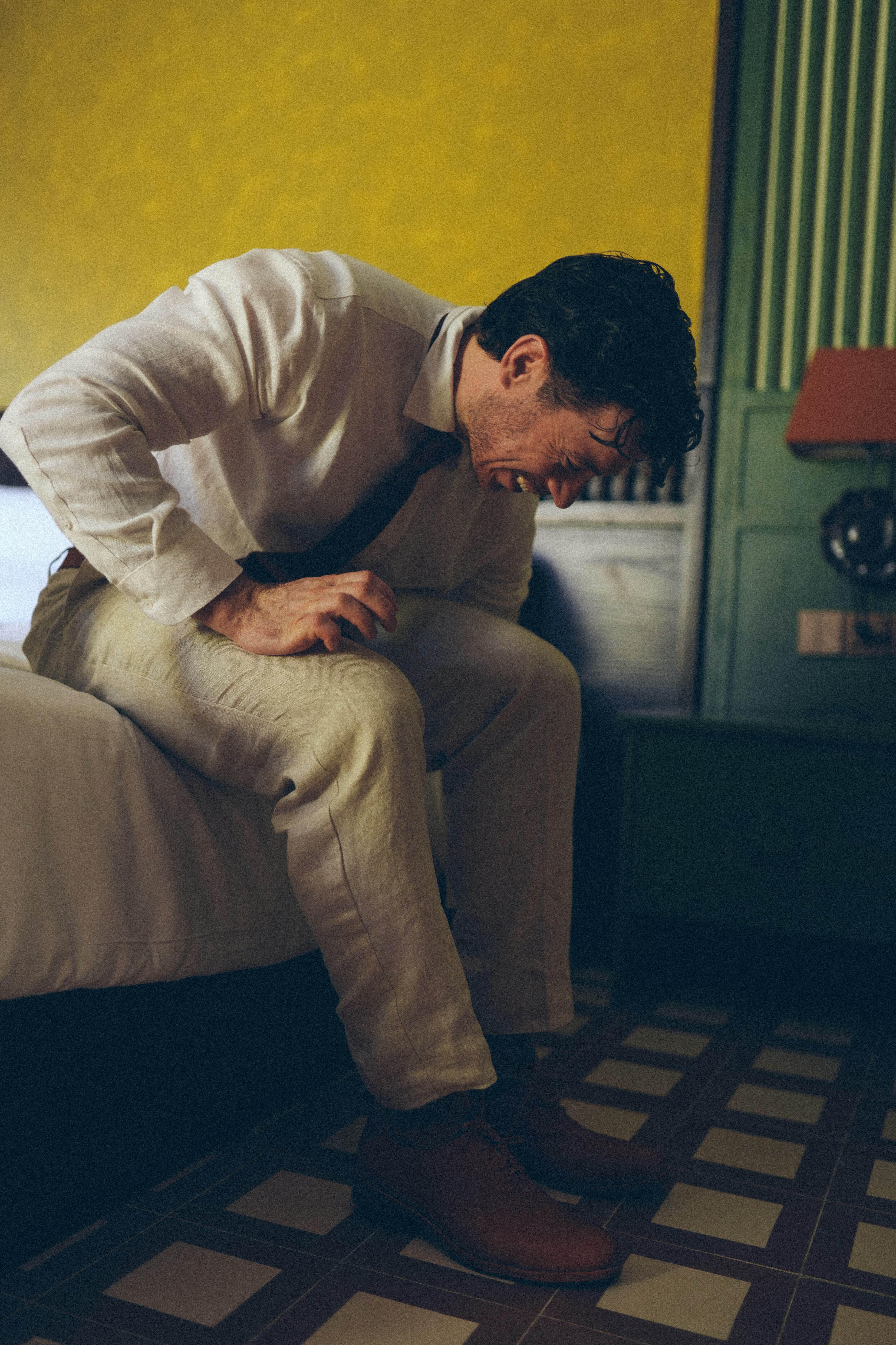 Man in suit sitting on bed, holding stomach