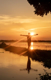 Man with arms outstretched at sunset over water