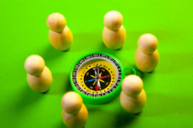 Wooden figures surround a green compass on a green surface