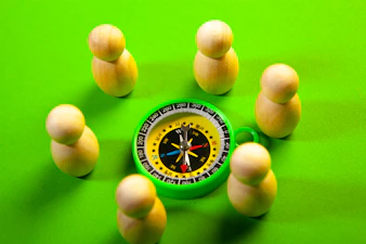 Wooden figures surround a green compass on a green surface