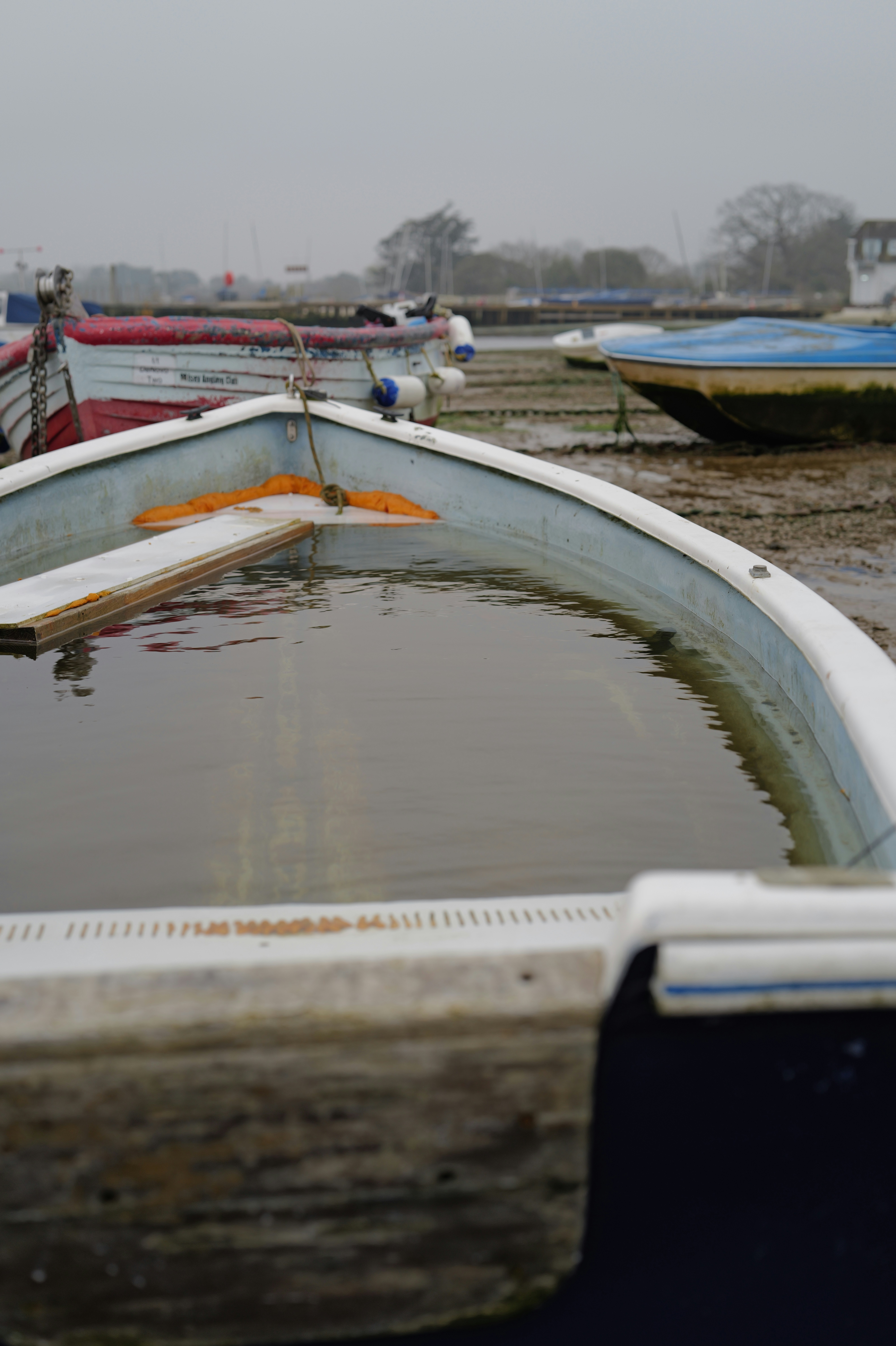 A boat filled with water sits on a muddy shore.