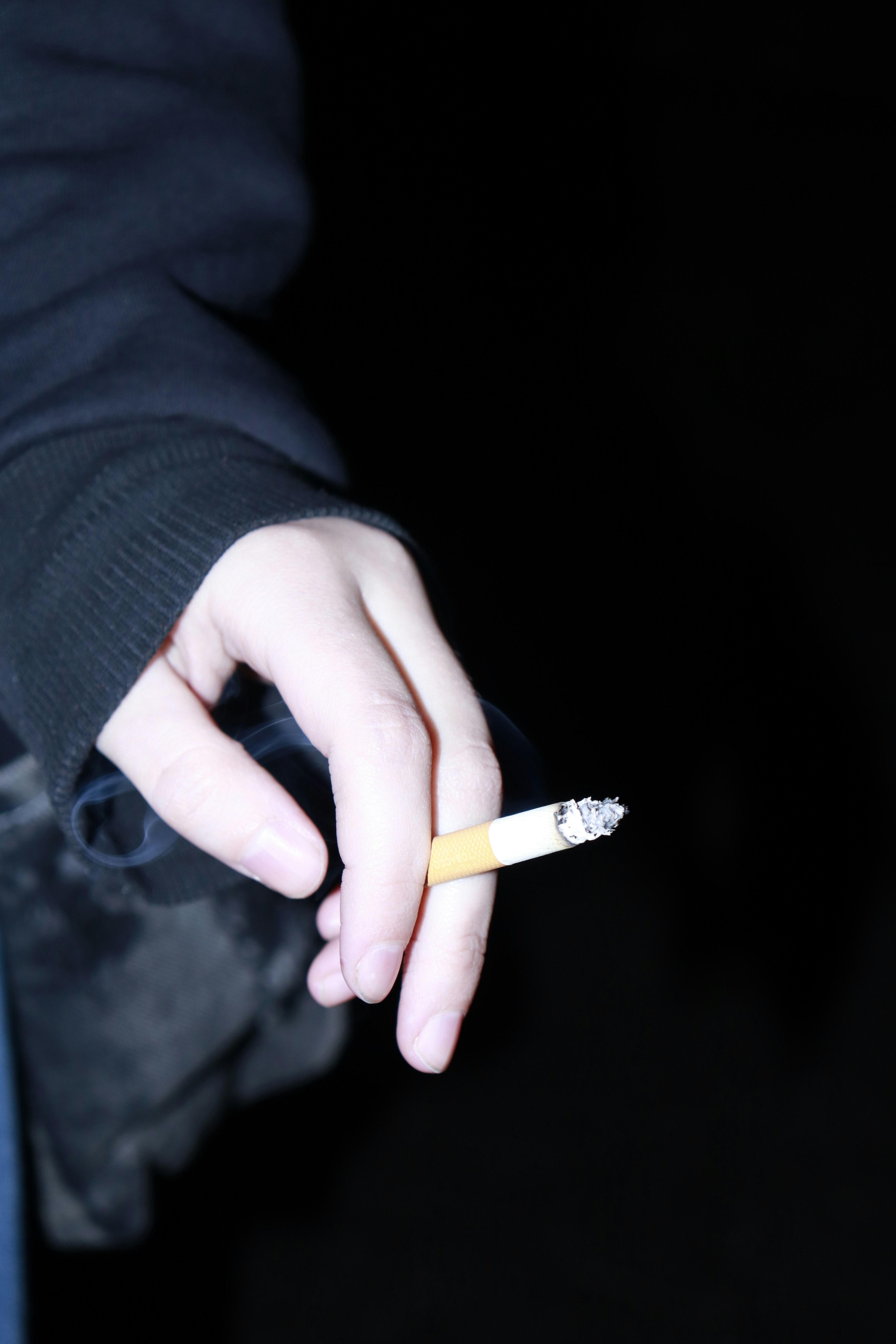 Una mano che tiene una sigaretta accesa con fumo.