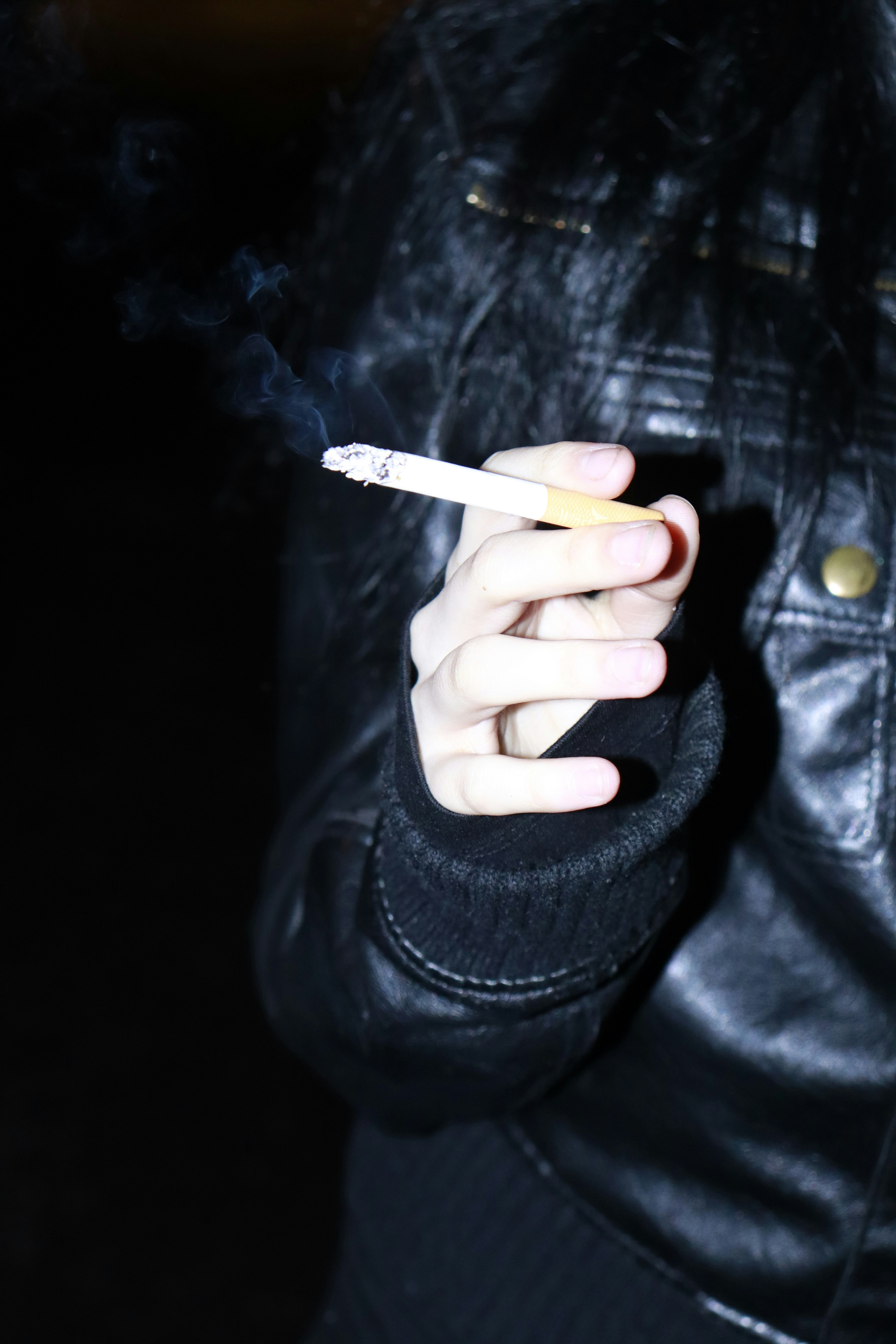 Una persona con una giacca di pelle che fuma una sigaretta.