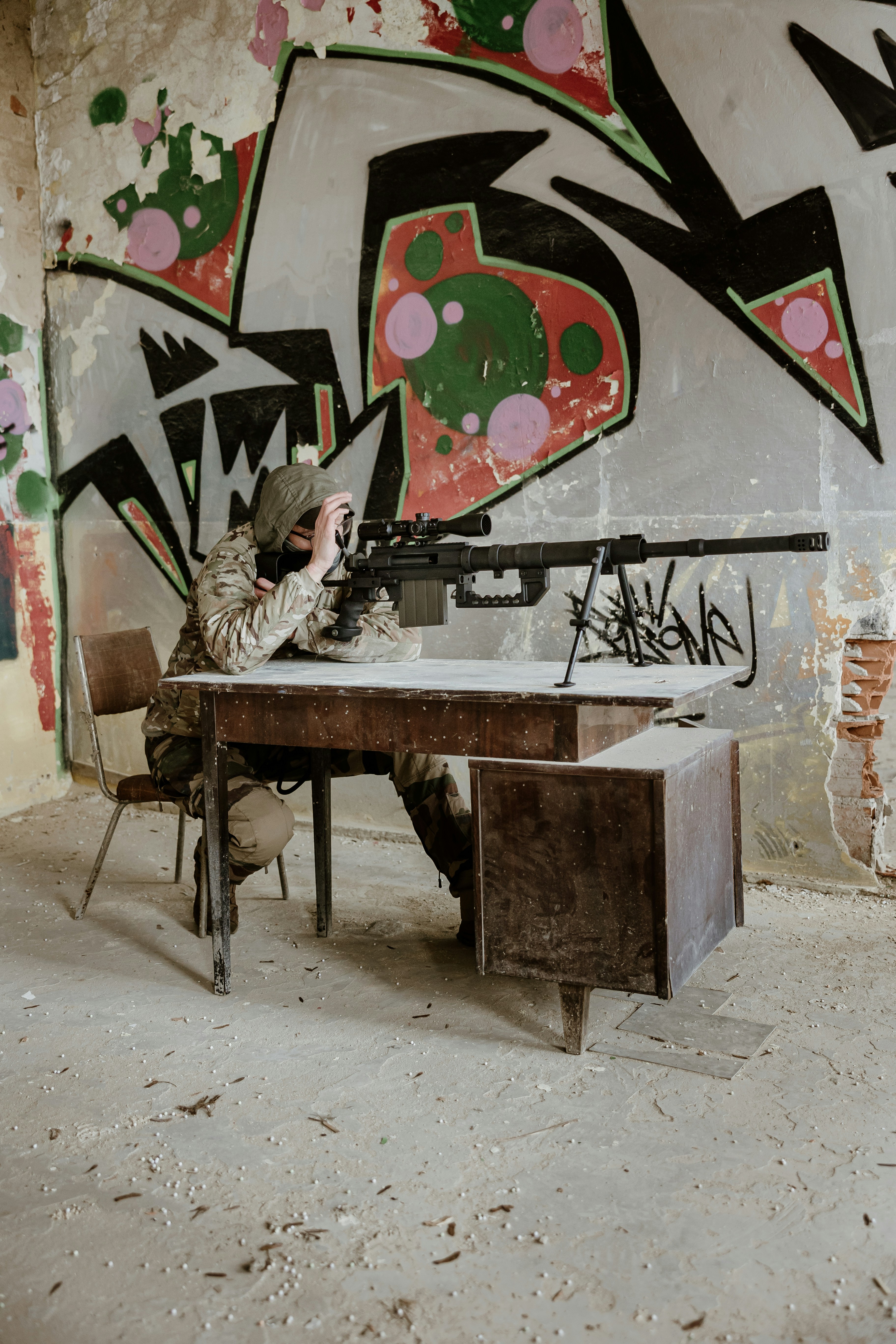 Soldat zielt mit Scharfschützengewehr hinter dem Schreibtisch mit Graffiti