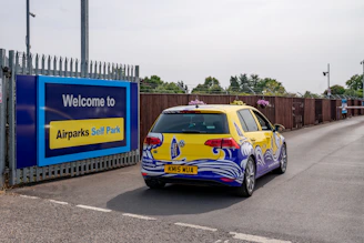 A yellow car with colorful graphics drives towards an entrance.