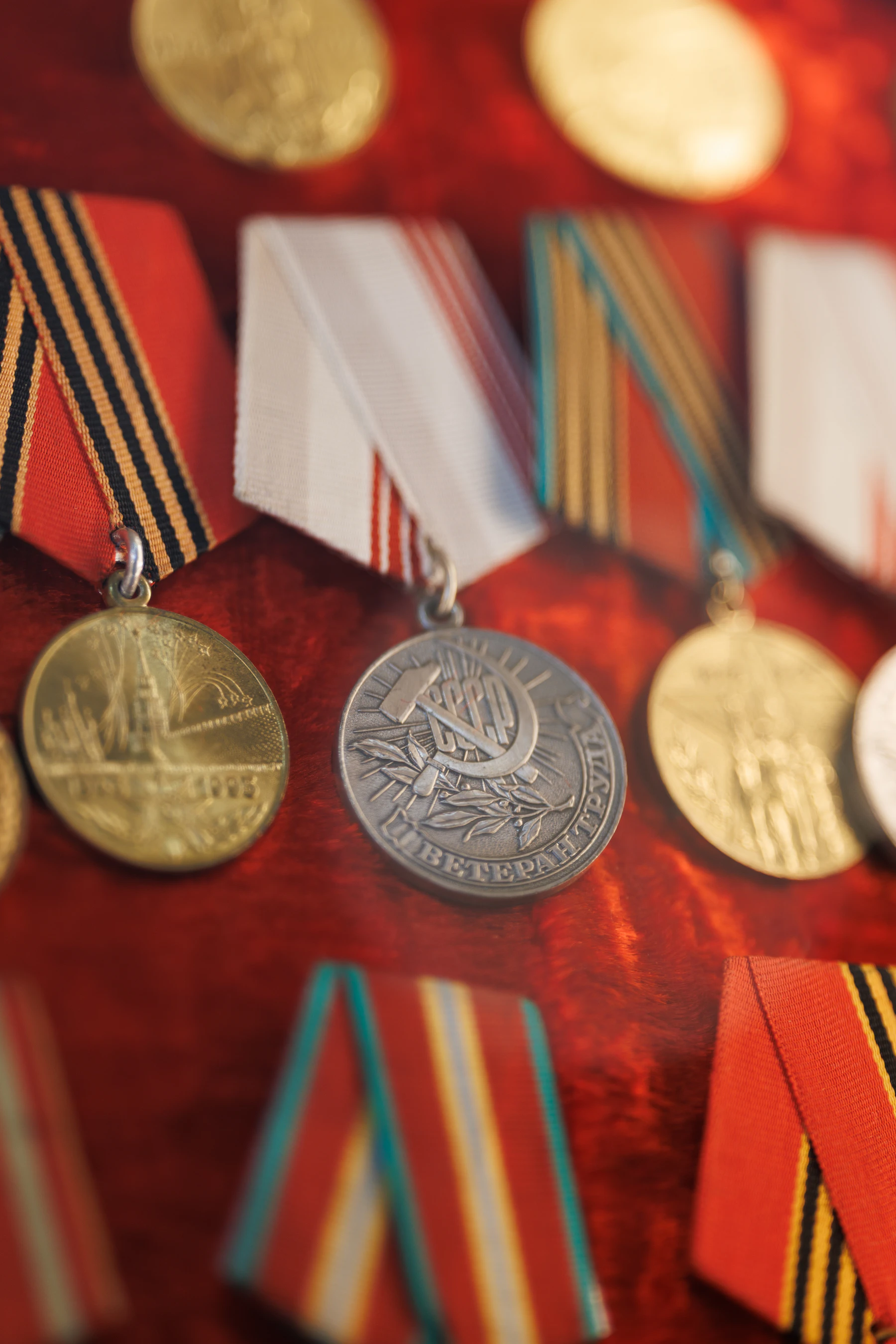 Close-up of a silver medal and two brass ones hanging from striped ribbons against red velvet