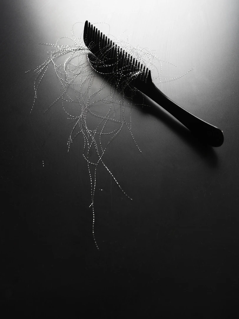 Black comb with strands of hair on dark surface