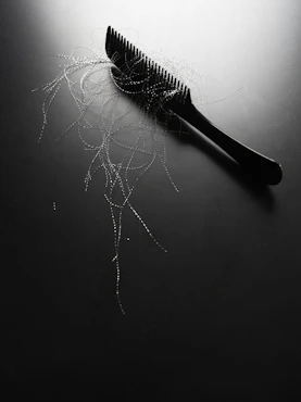 Black comb with strands of hair on dark surface