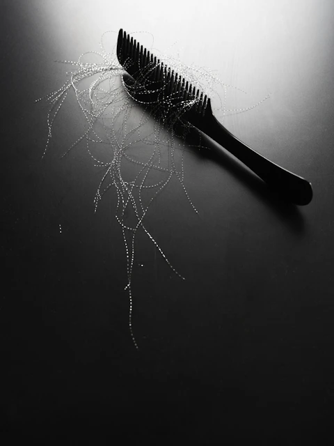 Black comb with strands of hair on dark surface
