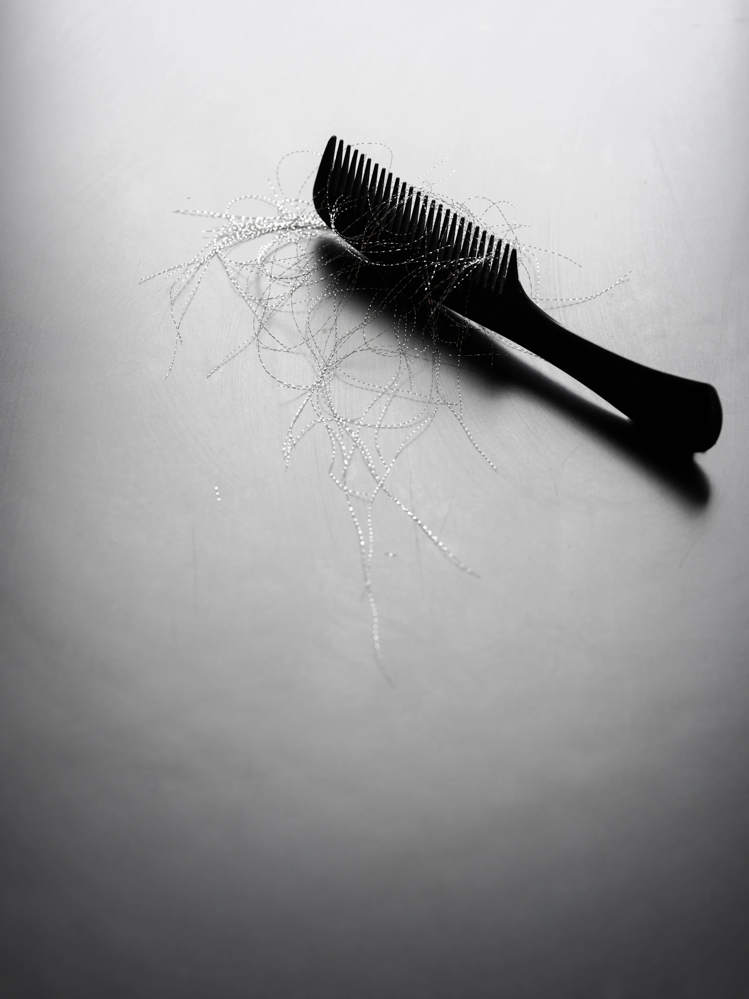 A black carbon comb lying on pale grey with a few cut hairs across it