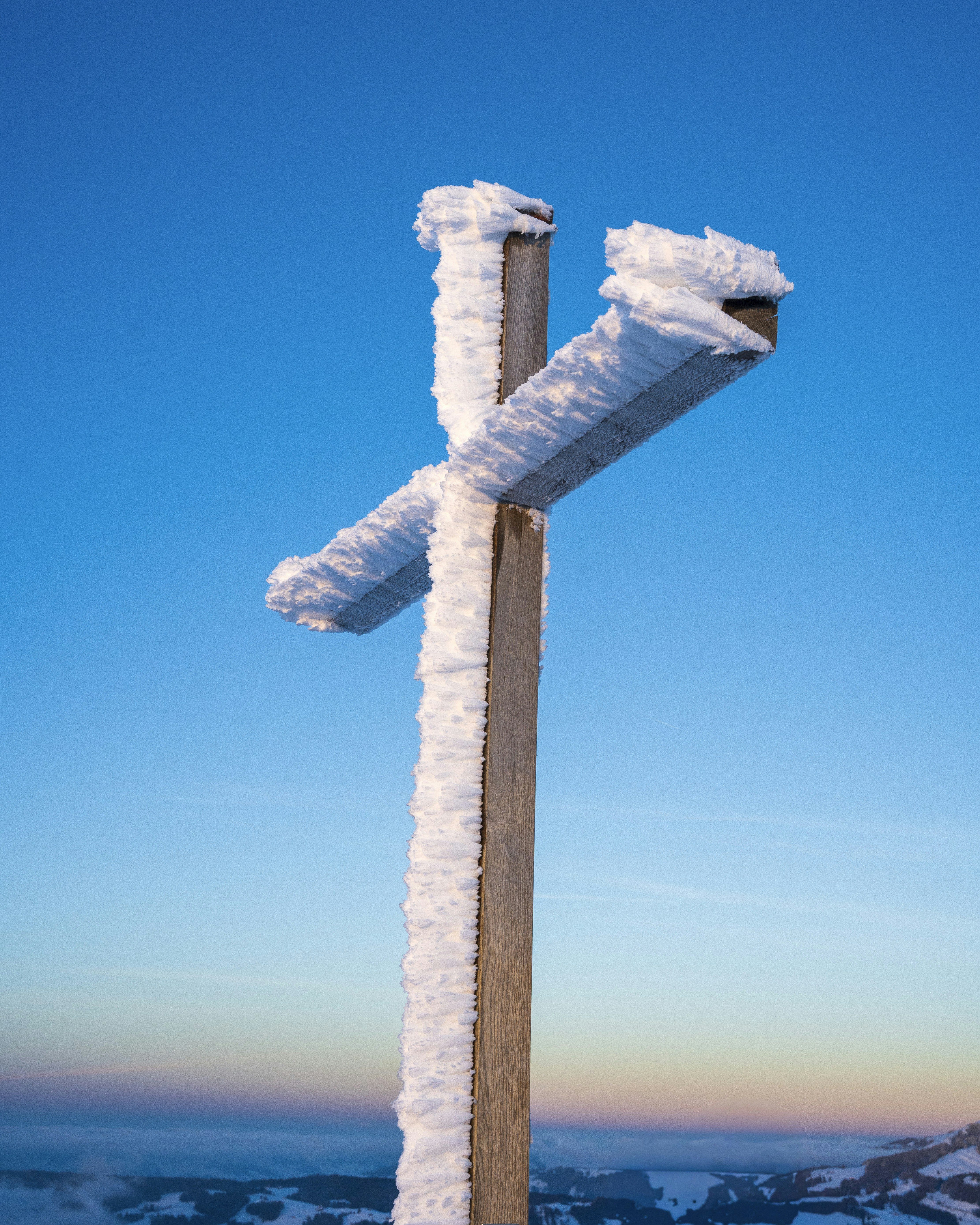 Wooden cross covered in snow against blue sky